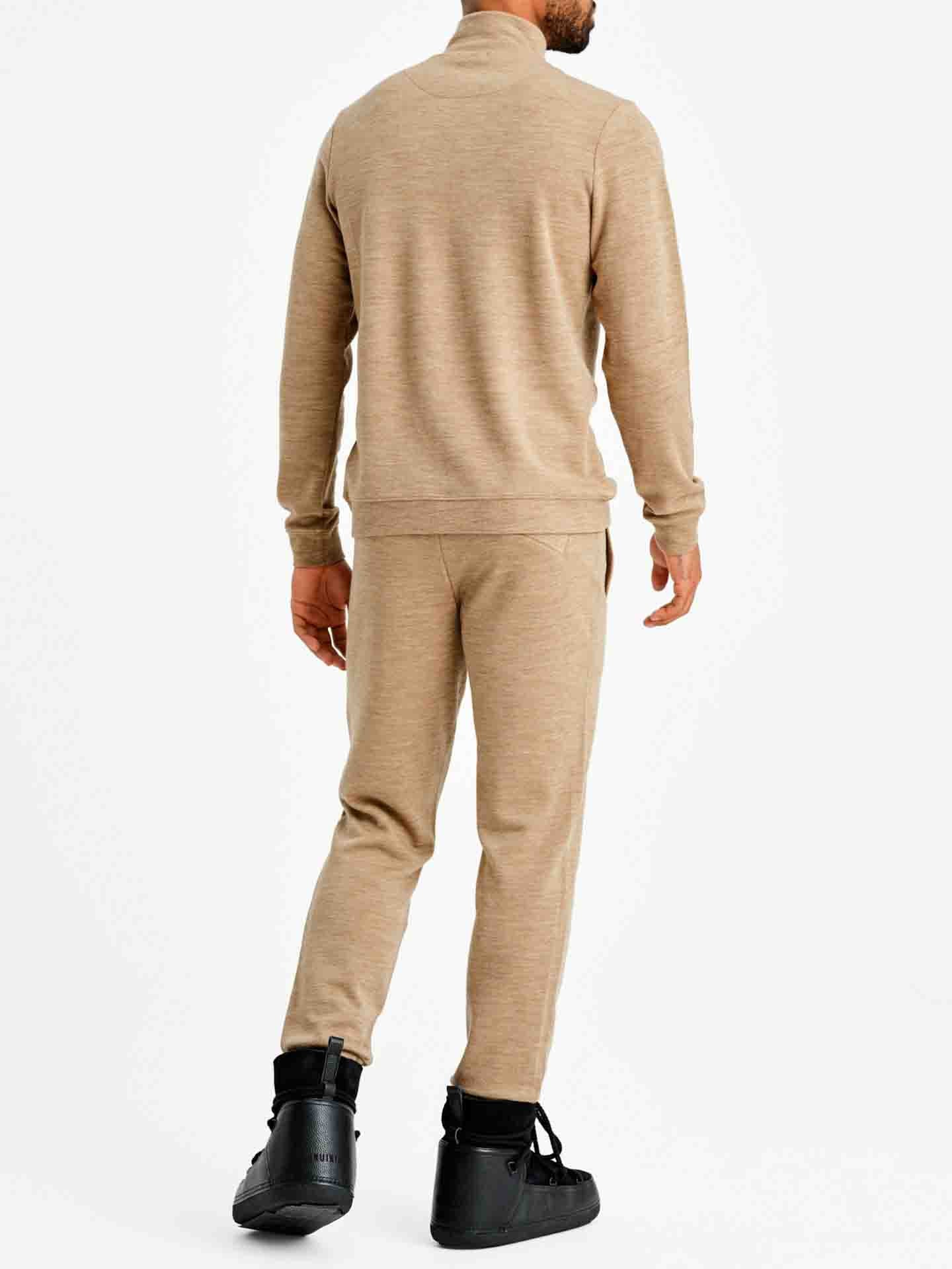 A person stands facing away, wearing the Tind 1/4 Zip Sweater Men in Camel by We Norwegians, along with black high-top sneakers. The sweater has a relaxed fit with a subtle texture, complemented by sleek, modern design sneakers. The background is plain white.