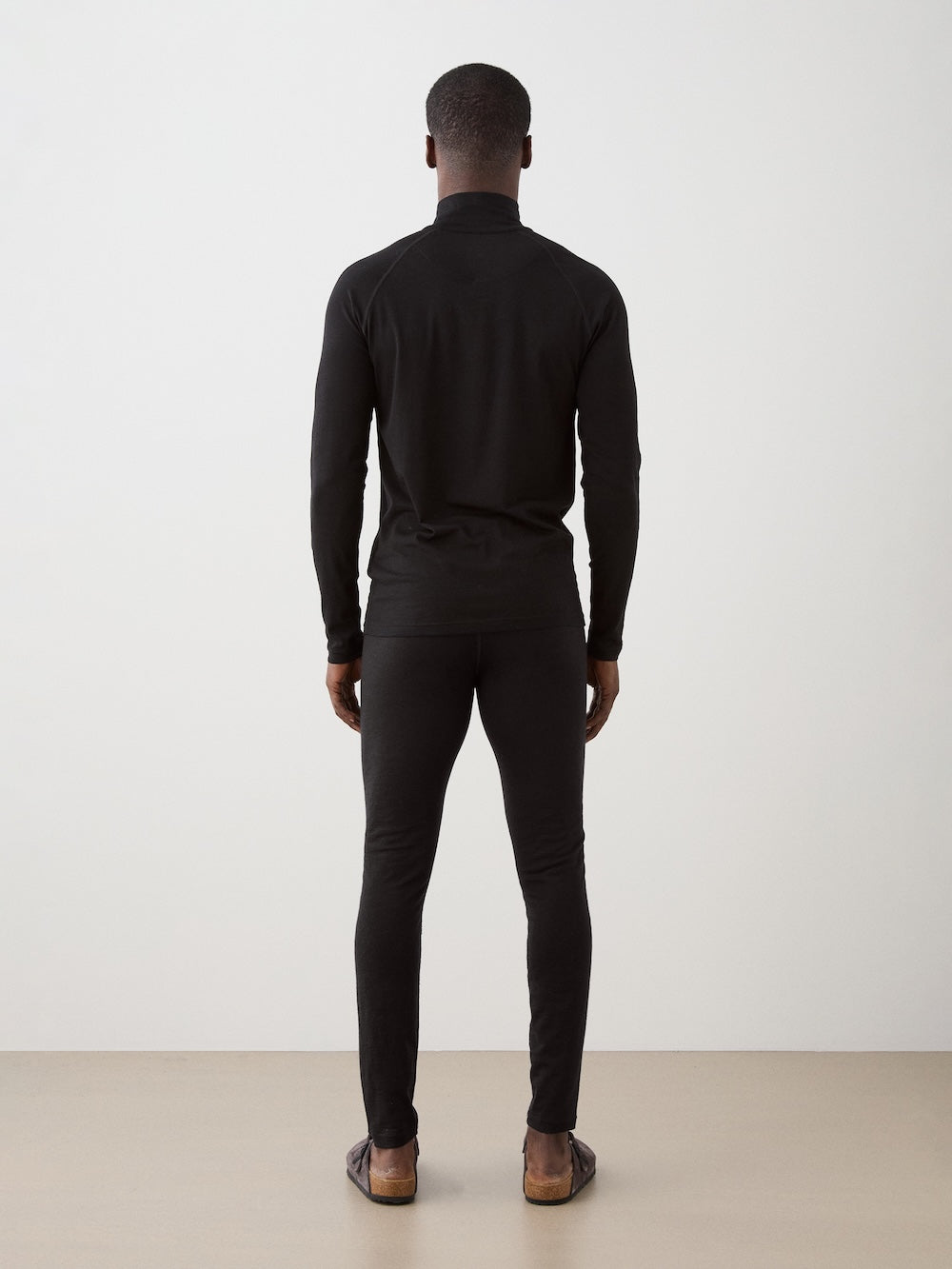 We Norwegians | FW25 | Mens Sno Zip-up_Black | A close fit, breathable base layer with a stand collar, 1/4th zipper opening and long sleeves on an off-white background | Back