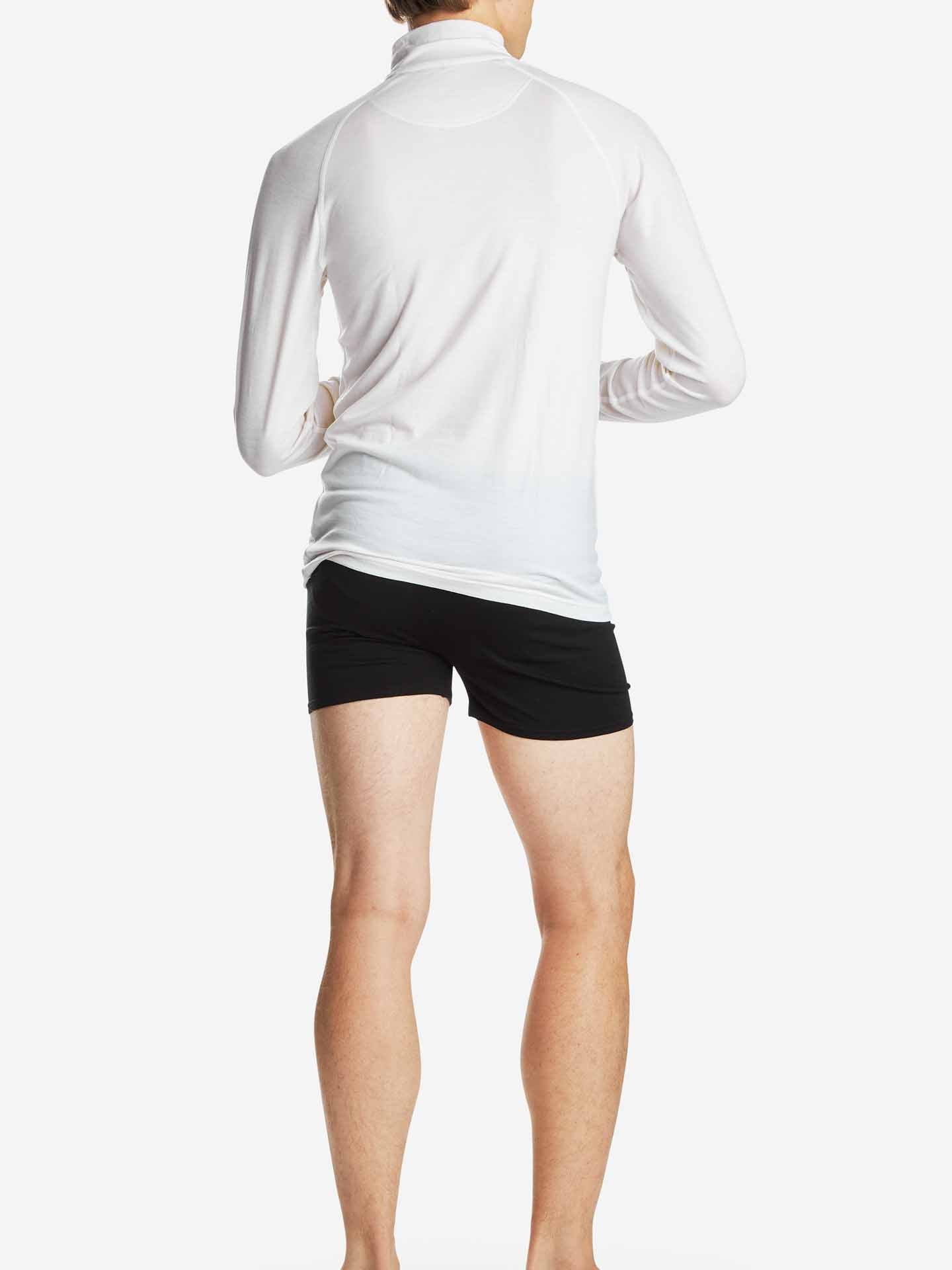 Person wearing a white Sno Merino Zip Up Men shirt by We Norwegians and black shorts, standing barefoot and facing away from the camera against a plain white background.