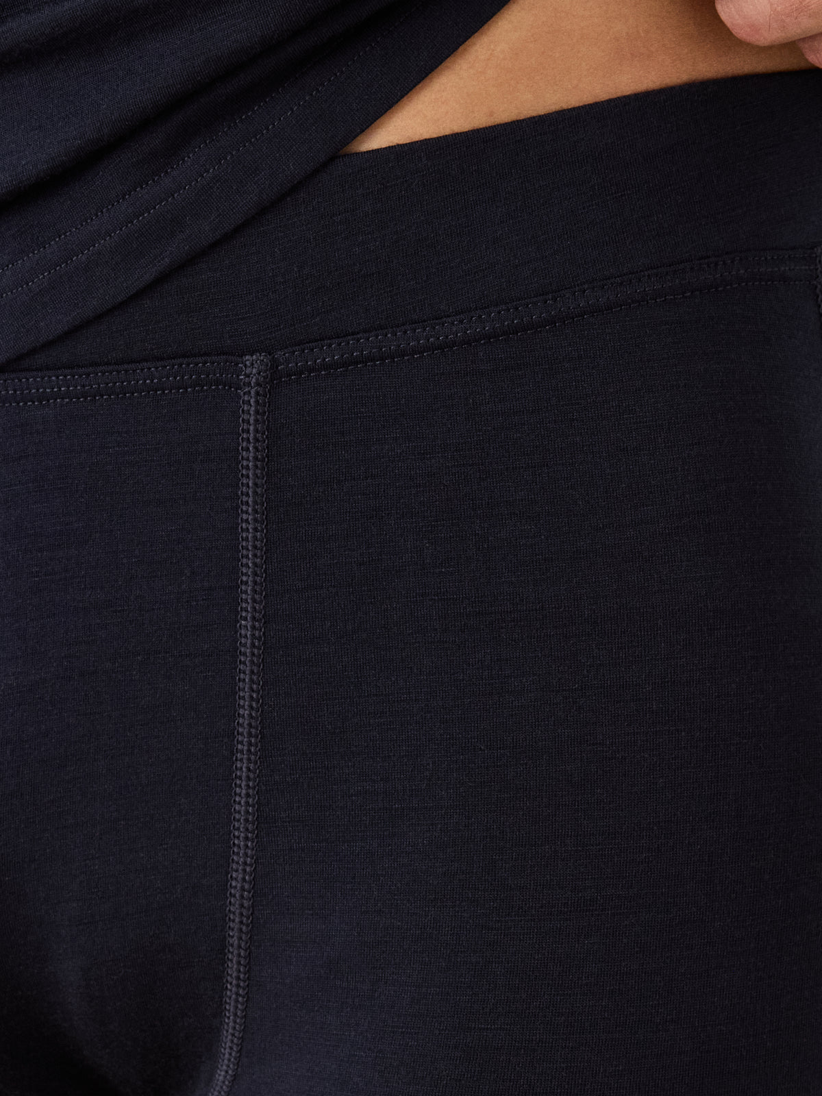 A close-up of a person wearing We Norwegians Sno Merino Long Johns Bottoms Men, featuring dark, fitted merino wool with visible seams and waistband against their skin.