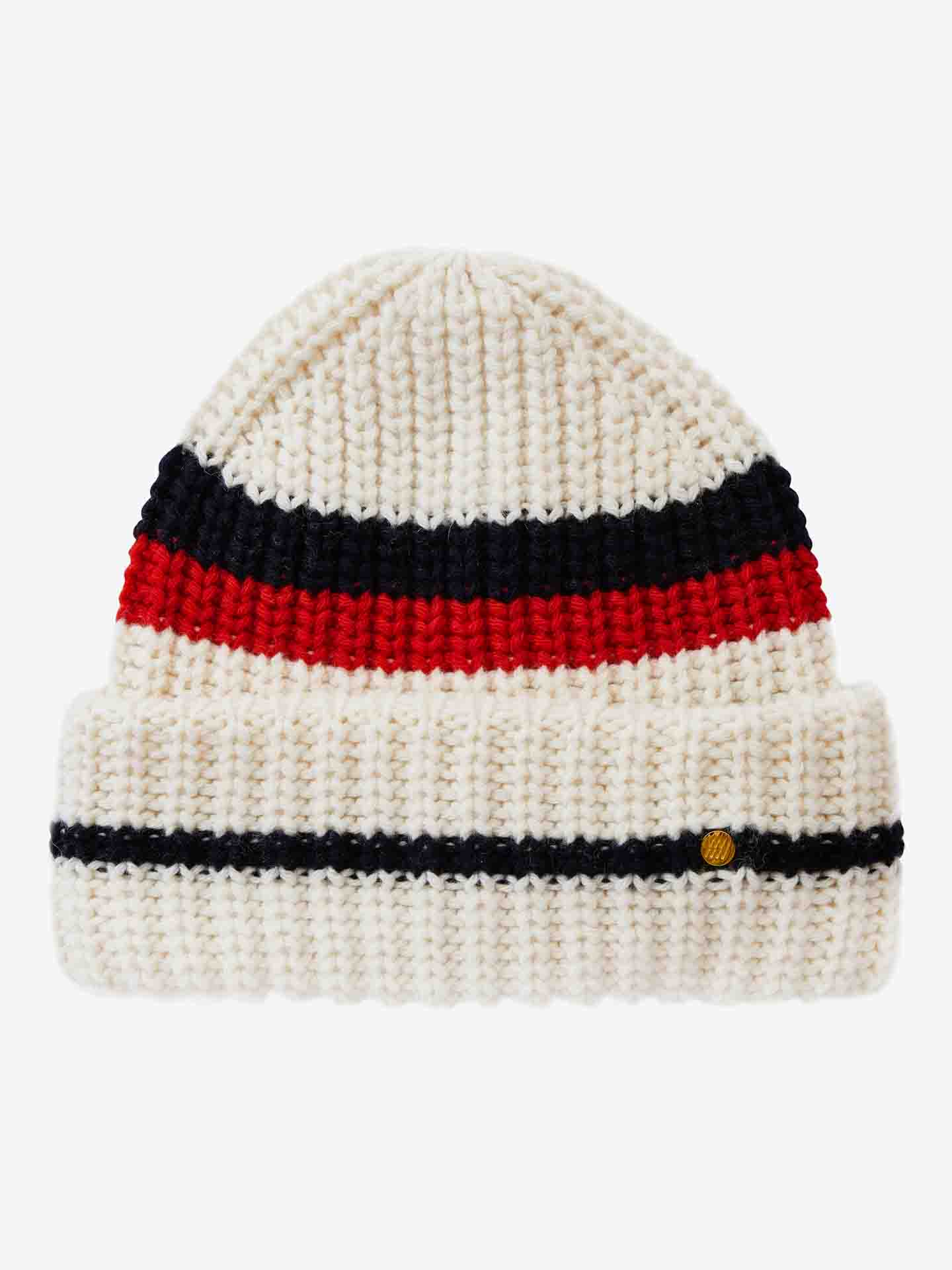 The Apres Ski Hat Women by We Norwegians is a knitted white beanie adorned with a wide horizontal red stripe and a narrower navy blue stripe positioned above it. Drawing inspiration from 70's ski fashion, this hat features a folded brim with an additional horizontal navy blue stripe near the bottom. The brim is accented with a small, circular gold emblem.