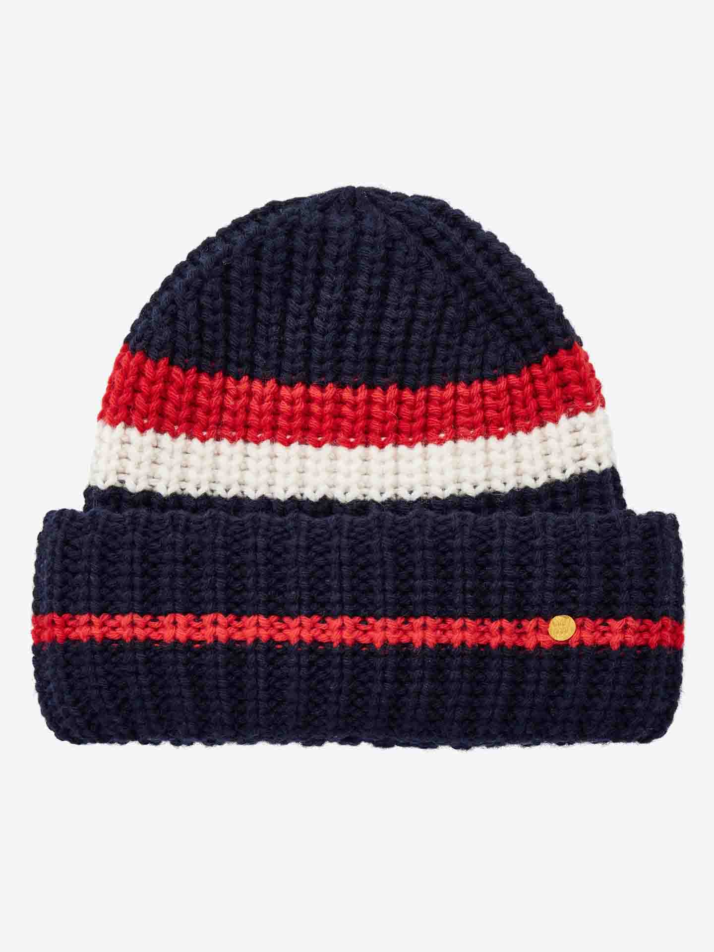 The Après Ski Hat Women by We Norwegians is a knitted beanie with a navy blue base, showcasing a red and white striped pattern near the top and a single red stripe around the brim. Inspired by 70s ski fashion, this hat is finished with a small, gold-colored button attached to the brim.