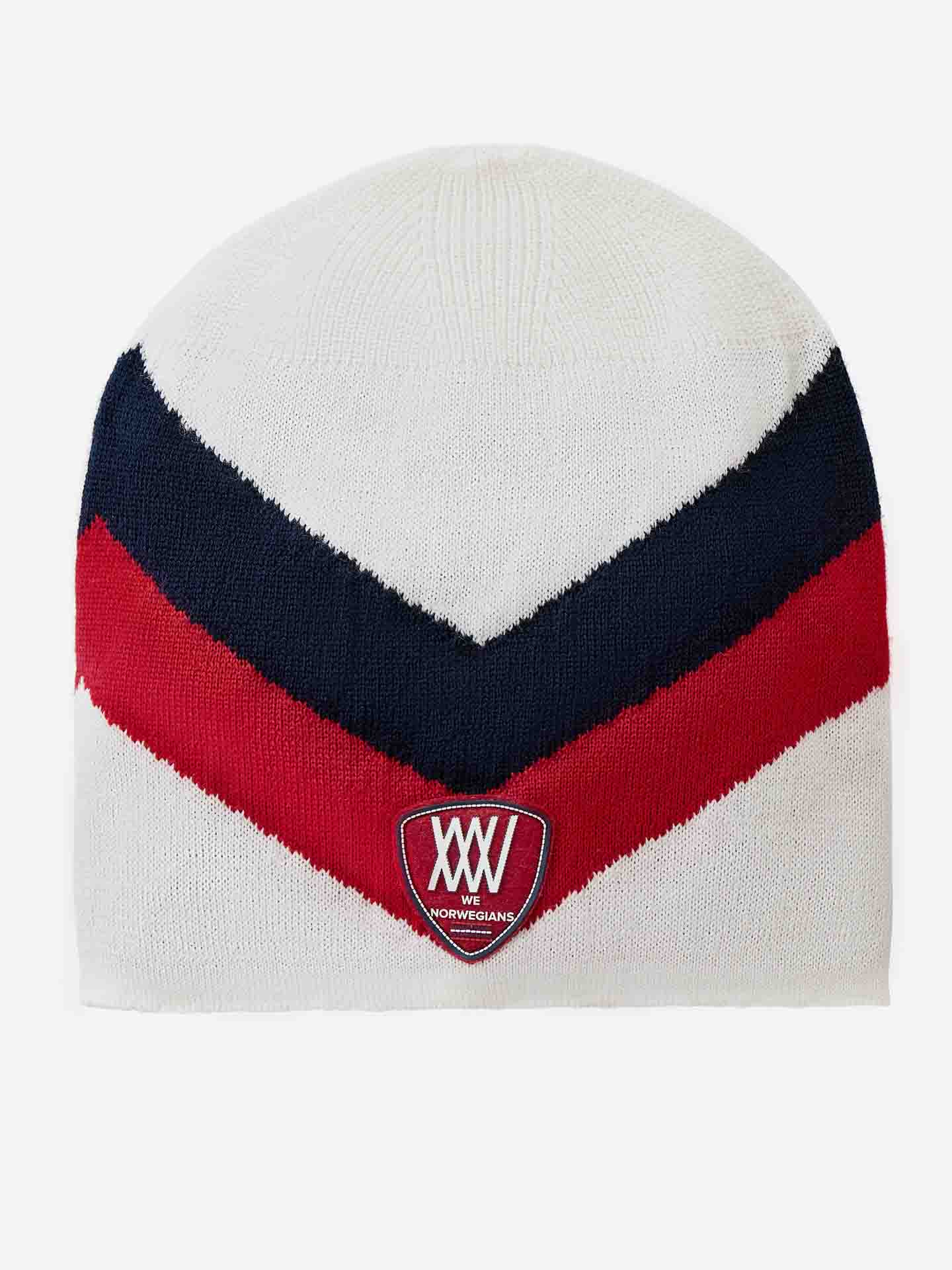 The Beito Hat by We Norwegians is a white knit beanie crafted from breathable Merino wool, adorned with V-shaped red and black stripes. It features a small embroidered badge near the bottom edge displaying the text "NORWEGIANS" and Roman numerals "XXV" in white on a red background, making it perfect for ski hat enthusiasts.