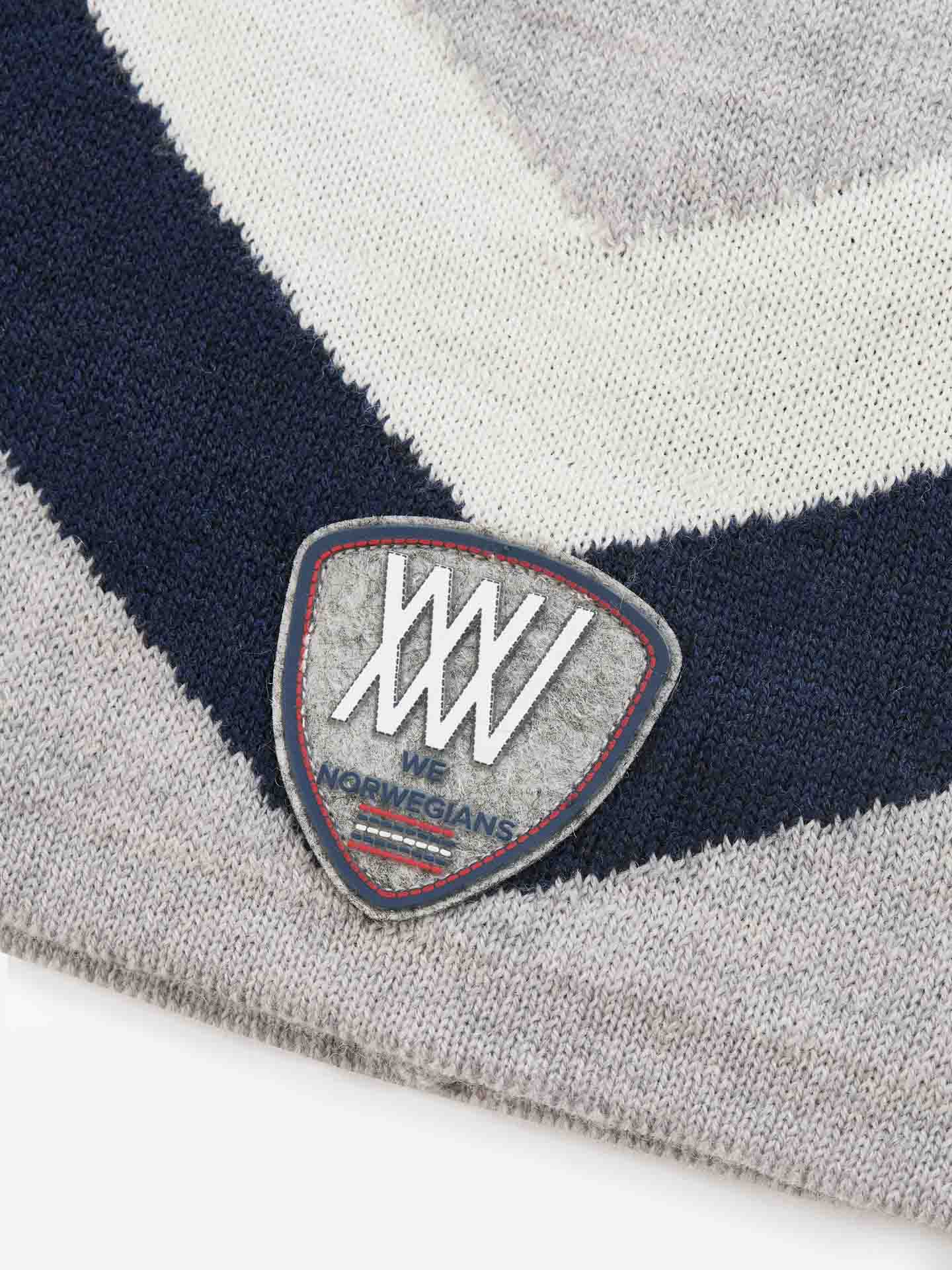 Close-up of a knitted fabric made from breathable Merino wool, featuring a triangular badge with intertwined "WW" letters and the text "WE NORWEGIANS." The Beito Hat fabric displays a diagonal pattern in light gray, dark blue, and cream shades. Ideal for ski hats.