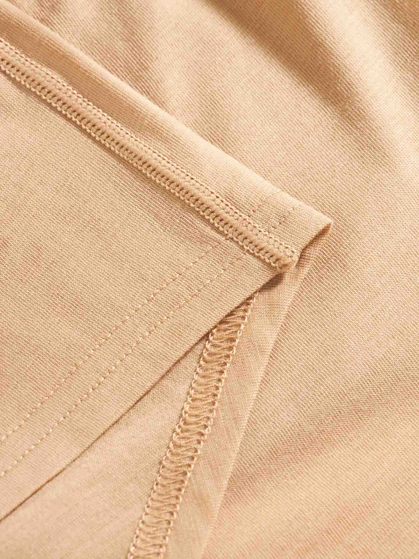 Close-up image of a beige fabric with visible seaming and stitching detail. The image showcases the texture and construction of the Sno Merino Hipster Women's super fine merino wool, highlighting its smooth and clean finish. Perfect for Scandinavian Luxury base-layers, this We Norwegians material offers a breathable fabric experience.