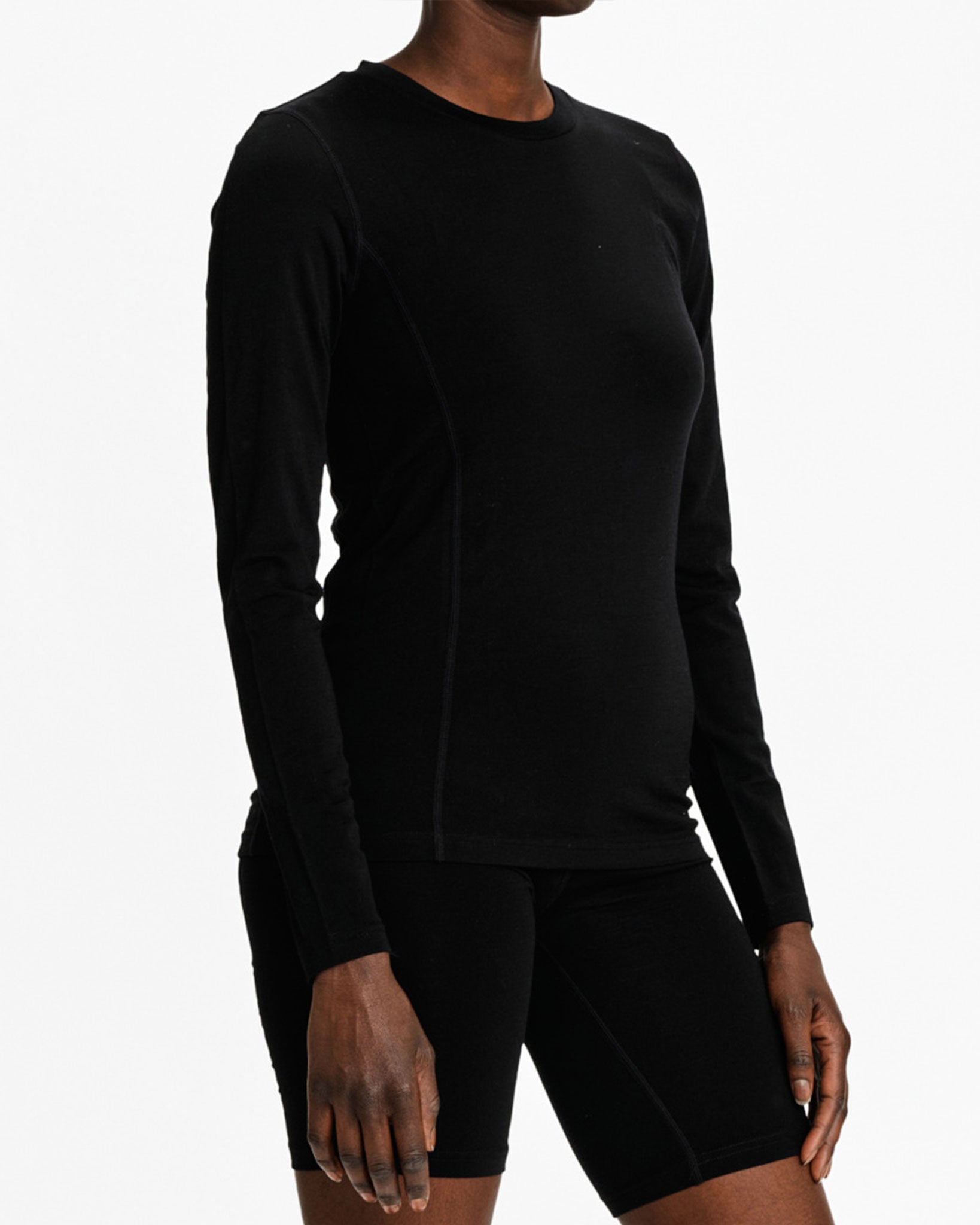 A person dressed in a We Norwegians Sno Merino Crewneck Women top and black shorts, made from super fine merino wool, stands against a white background. The outfit is sporty and minimalistic, with the person's head not visible.