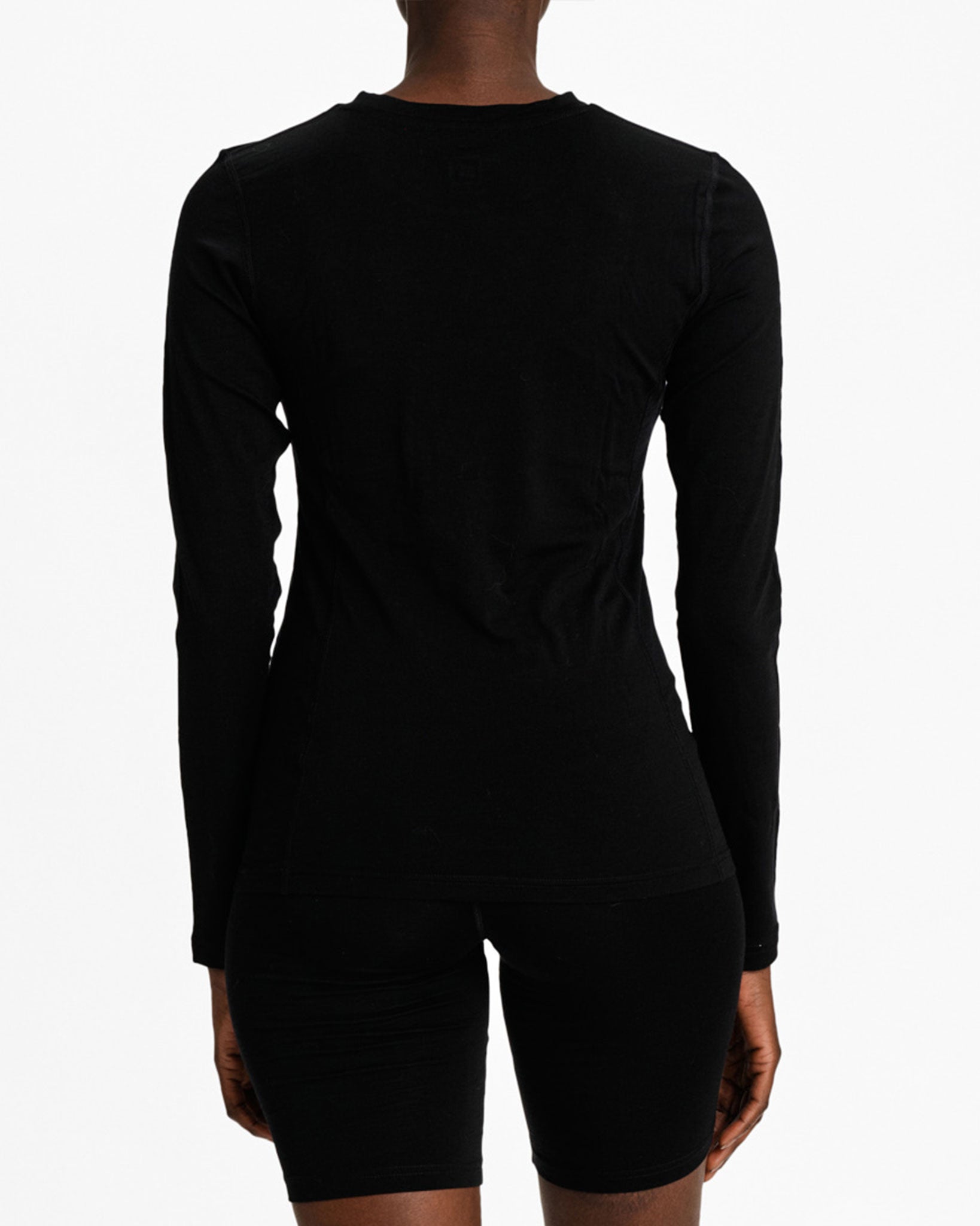 Rear view of a person wearing We Norwegians Sno Merino Crewneck Women in black and black shorts, made from superfine merino wool, against a plain white background.