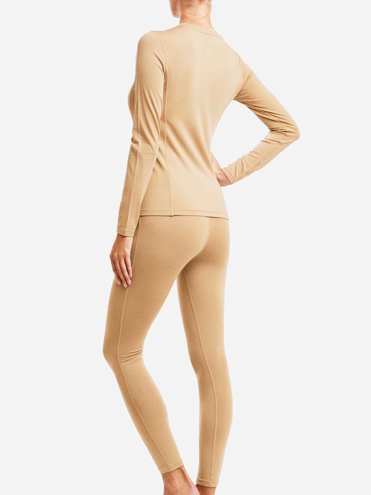 A person wearing a fitted, long-sleeve Sno Merino Crewneck top and matching leggings from We Norwegians stands barefoot on a white background. Shown from the back, with one hand resting on their hip, they embody Scandinavian Luxury base-layers at their finest.