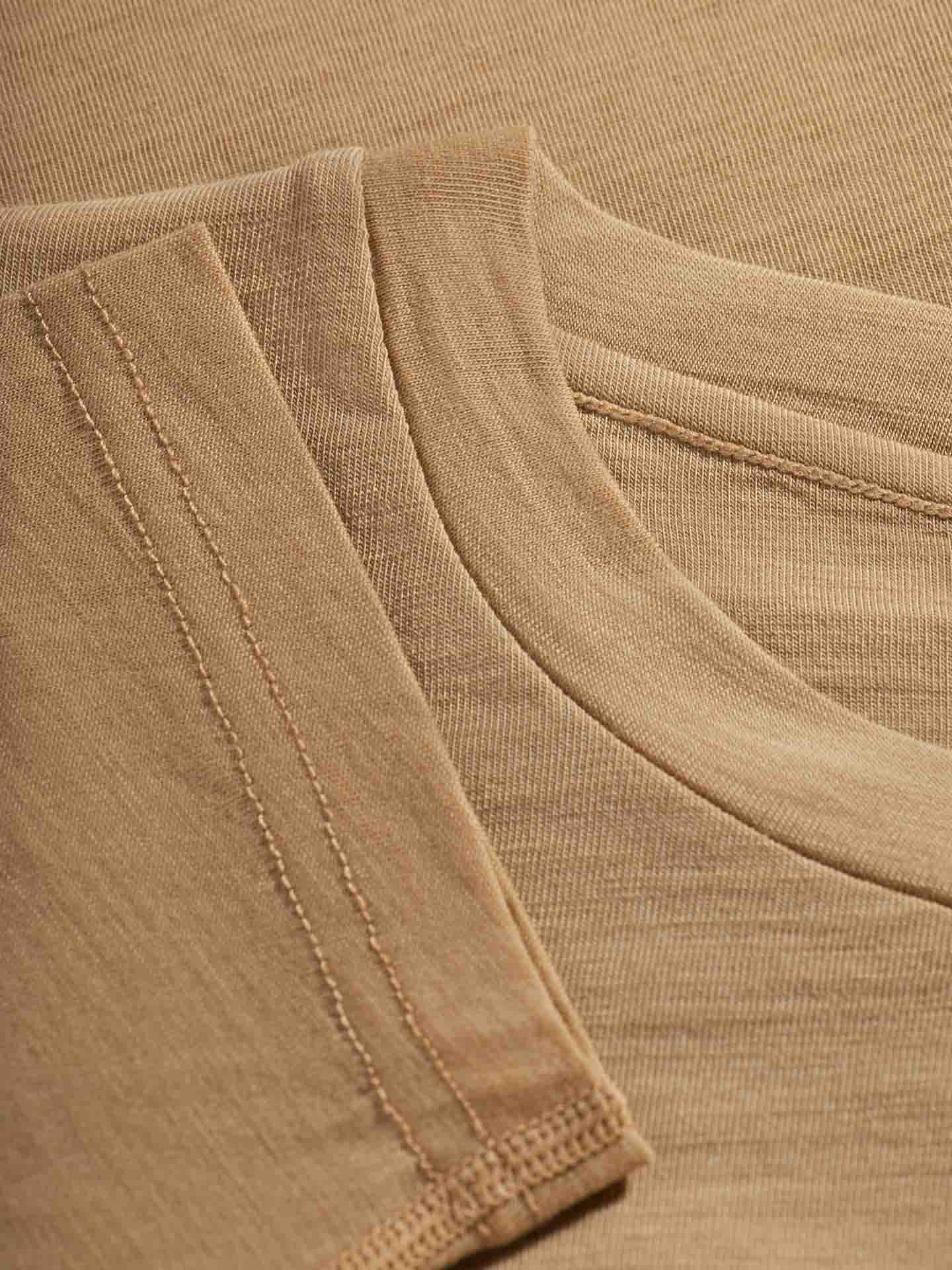 Close-up of a beige ribbed fabric with visible overlapping seams and stitching detail. The image showcases two areas where the Sno Merino Crewneck Women by We Norwegians, made of superfine merino wool, join together, highlighting the texture and craftsmanship in the stitching.