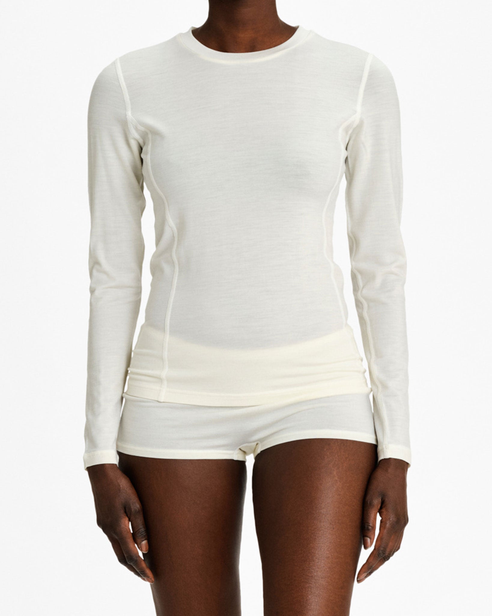 Against a plain white background, a person wears the We Norwegians Sno Merino Crewneck in cream-colored super fine merino wool. Matched with seamless shorts, this Scandinavian luxury base-layer provides a comfortable and fitted look while the individual stands neutrally.