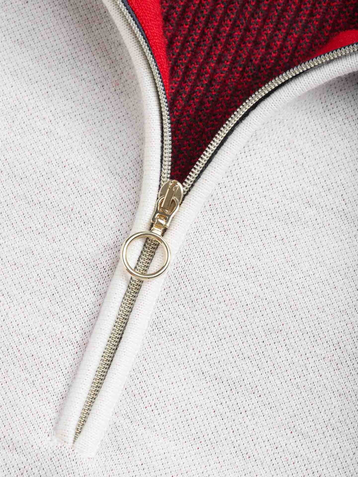 Close-up of a partially unzipped Hafjell Zip Up Women sweater from We Norwegians, featuring a metallic zipper. The zipper reveals red, textured fine merino wool underneath, creating a striking contrast between the outer white fabric and the inner red layer. Expertly crafted by skilled Italian knitters, the zipper pull is designed with a circular ring.