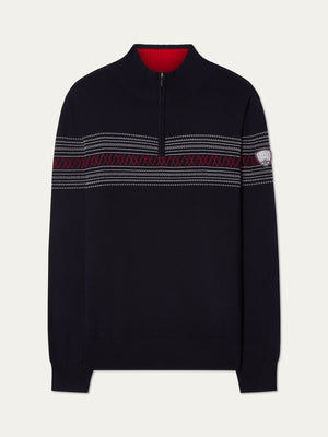The We Norwegians Signature Zip Up Men is a navy blue pullover sweater featuring a half-zip collar, red interior lining, and a patterned stripe across the chest inspired by the classic Norwegian Setesdal design. Crafted from washable merino wool, it also includes a small patch on the left sleeve.
