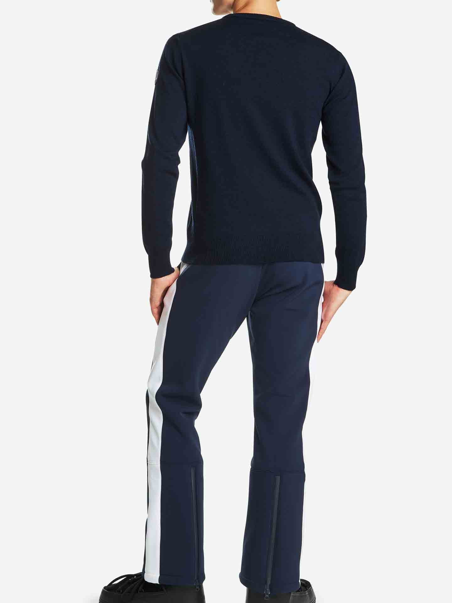 Rear view of a person standing against a white background, wearing the Signature Crewneck Men by We Norwegians paired with dark pants featuring a white vertical stripe down each leg. The individual is also wearing dark shoes, reminiscent of traditional Norwegian heritage styling seen in Setesdal base layers.