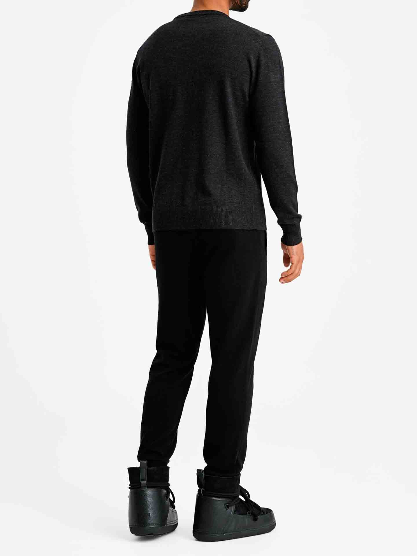 A man stands against a plain white background, seen from the back. He is wearing the Signature Crewneck Men sweater by We Norwegians, paired with black pants and black high-top sneakers. He has light skin and short hair, reflecting his Norwegian heritage. His right arm hangs by his side, while his left hand is slightly away from his body.