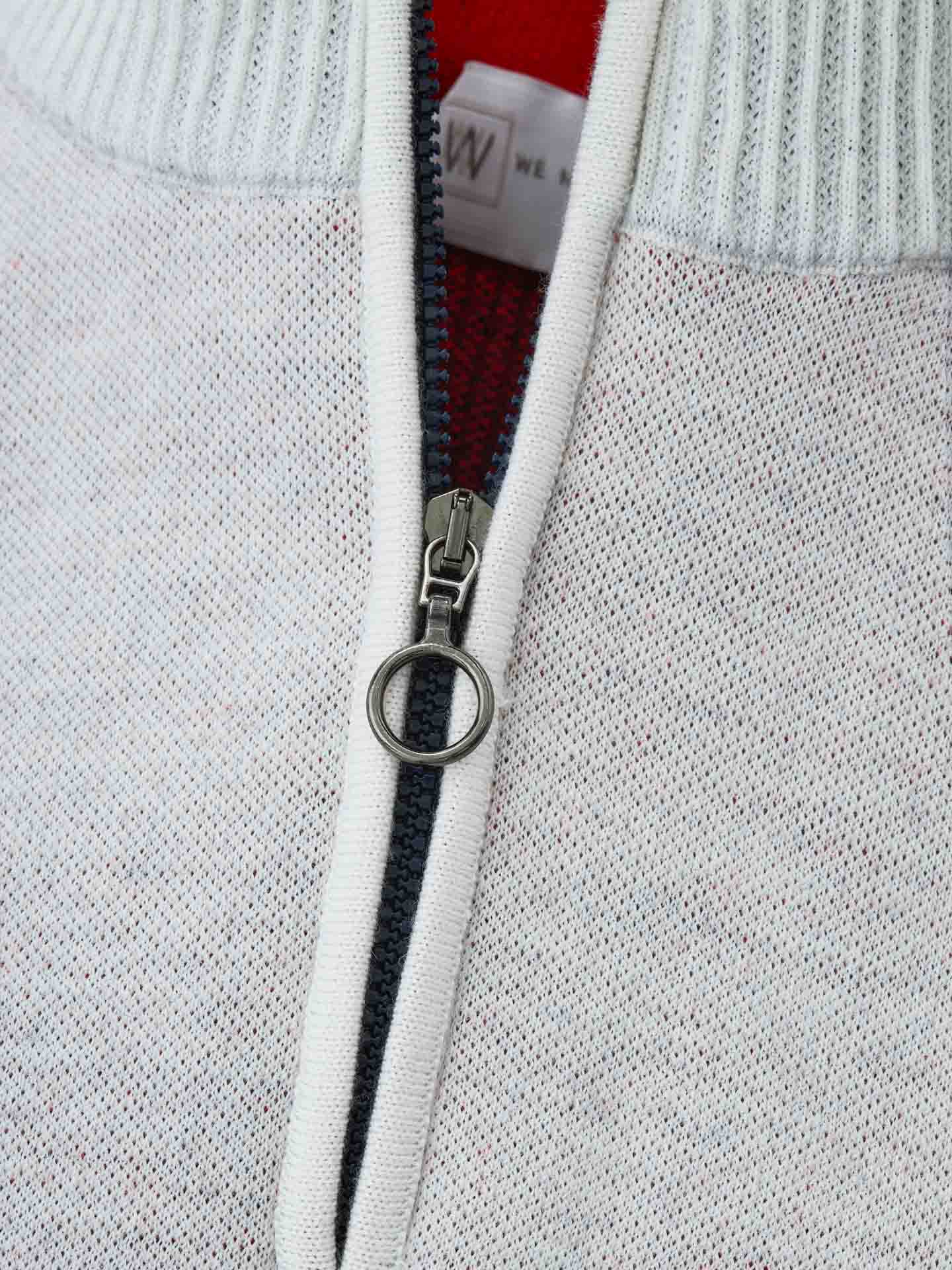 Close-up image of the Hafjell Zip Up Men ski sweater by We Norwegians. The white zipper is partially unzipped, revealing a red inner lining and a tag with a visible "W." Crafted by Italian knitters, the upper collar is ribbed, adding texture contrast to the smooth 100% fine merino wool fabric of the sweater.