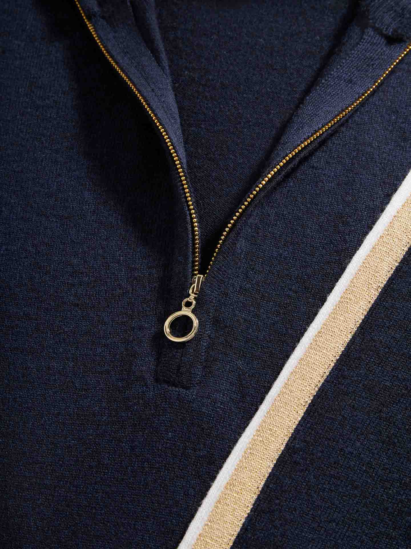 Close-up of a dark blue Geilo Zip Up Women jacket by We Norwegians, featuring a gold zipper and a white and gold diagonal stripe on the Merino Wool fabric. The image showcases the texture and details of the material—perfect for après-ski wear.