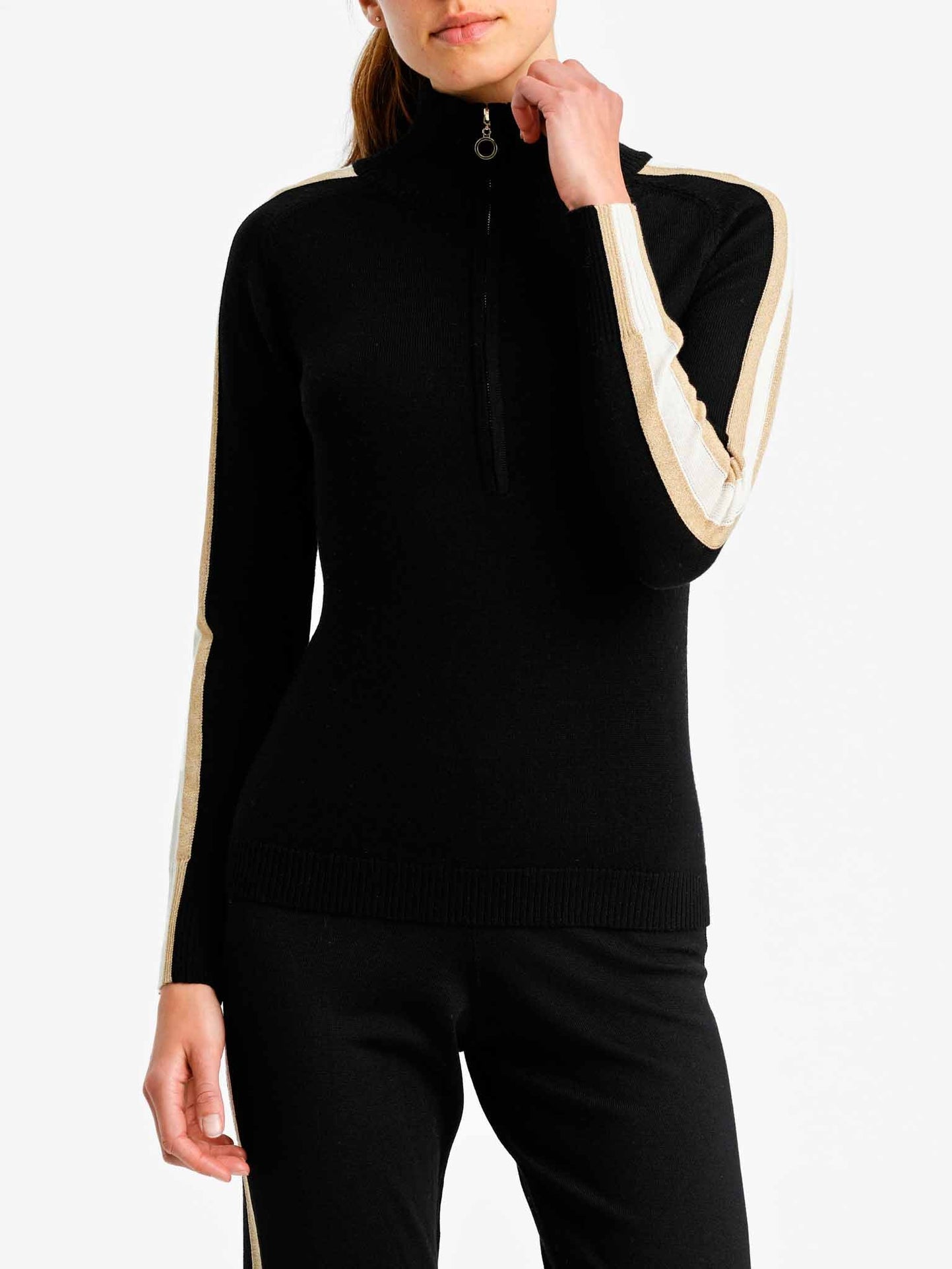 A person is wearing a Geilo Zip Up Women long-sleeve top by We Norwegians in black, featuring white and beige stripes along the sleeves. The person is also dressed in matching black pants. The outfit exudes a sporty, casual style ideal for après ski activities. The person's face is not visible in the image.