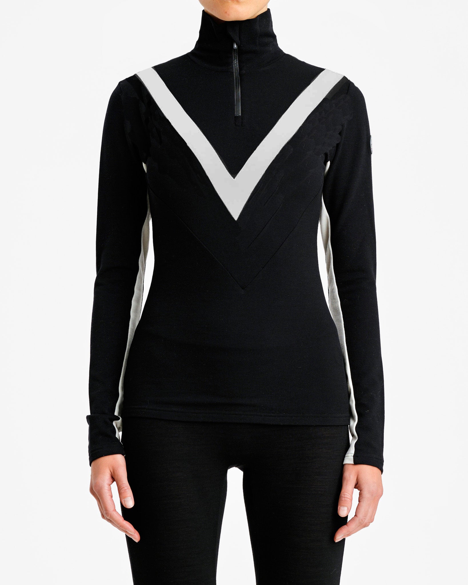 A person wearing the Voss Chevron ZipUp Women from We Norwegians, a long-sleeve black ski top made from Super Fine Merino wool with a high collar and front zipper. The top showcases a large white V shape on the chest and white panels along the sides, exuding retro vibes as they stand against a plain white background.