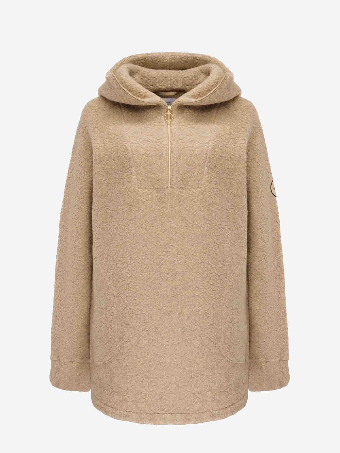 This is the Alta Shearling Hoodie Women by We Norwegians, a beige, long-sleeve fleece pullover featuring a quarter-zip front, hood, and two front pockets. The fabric has a textured, fluffy appearance reminiscent of aprés ski wear. A small circular patch adorns the upper part of the left sleeve. The background is plain white.