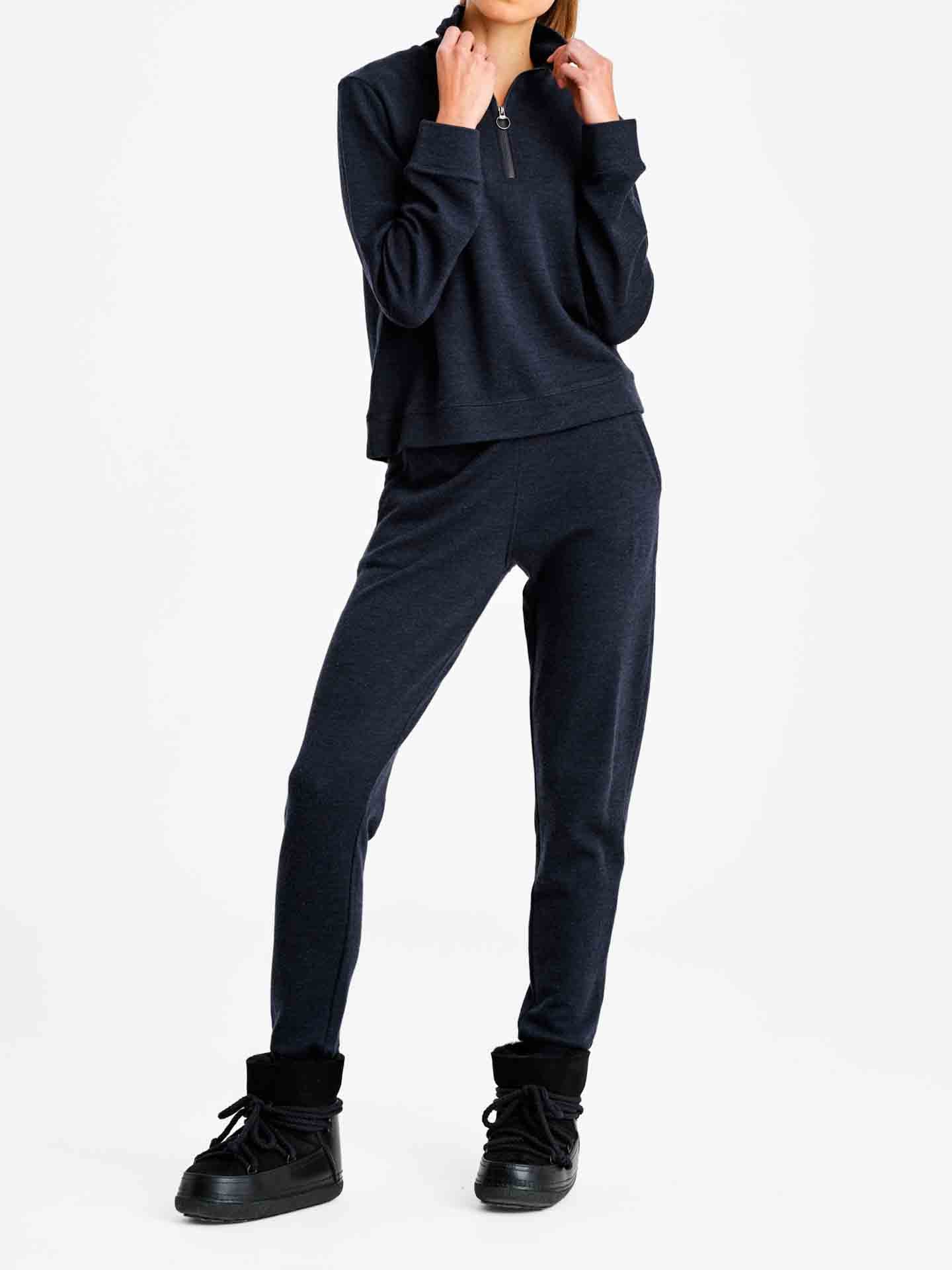 A person is wearing the We Norwegians Limited Time Bundle: Tind ZipUp & Tind Straight Leg Pant Women, featuring a long-sleeve, half-zip top and matching pants. They are also wearing black shoes with thick soles. The background is white, and the person’s face is not visible.