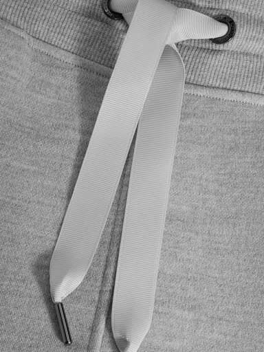 A close-up, black-and-white image of a drawstring on a pair of Tind Jogger Women Grey Melange from We Norwegians. The white drawstring is threaded through metal eyelets, tied in a simple loop. The fabric of these Merino wool sweatpants features a ribbed waistband, perfectly complementing their relaxed style.