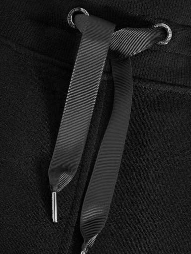 Close-up of black drawstring on Tind Jogger Women Black by We Norwegians. The drawstring, made of a ribbon-like material, threads through two metallic grommets. The fabric of the joggers is a jacquard structured knit, giving it a slightly textured look.