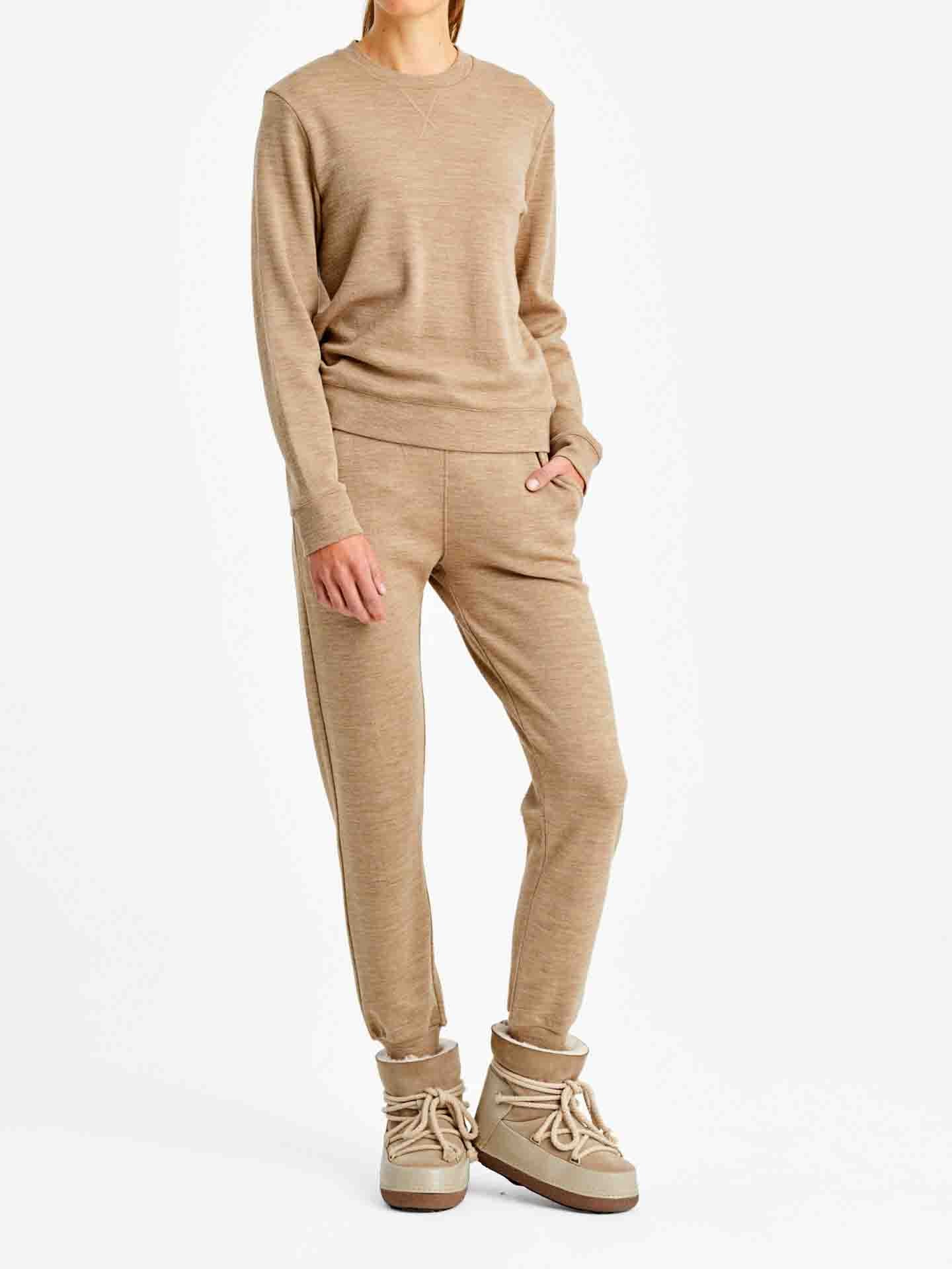 A person wearing a matching We Norwegians Limited Time Bundle: Tind Crewneck & Tind Joggers in beige, with their left hand in their pocket. They are also sporting light tan, high-top, lace-up boots. The background is plain white. The person's face is not visible.