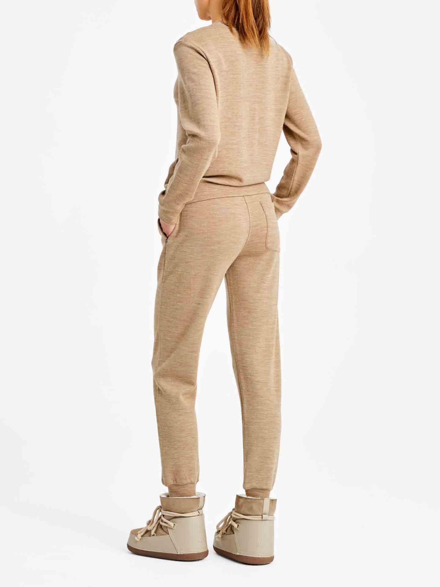 A person is seen from the back wearing a beige two-piece sportswear outfit, which includes the "Tind Crewneck Women Camel" by We Norwegians and fitted pants. The person also wears beige ankle boots with thick soles and laces. The background is plain white.