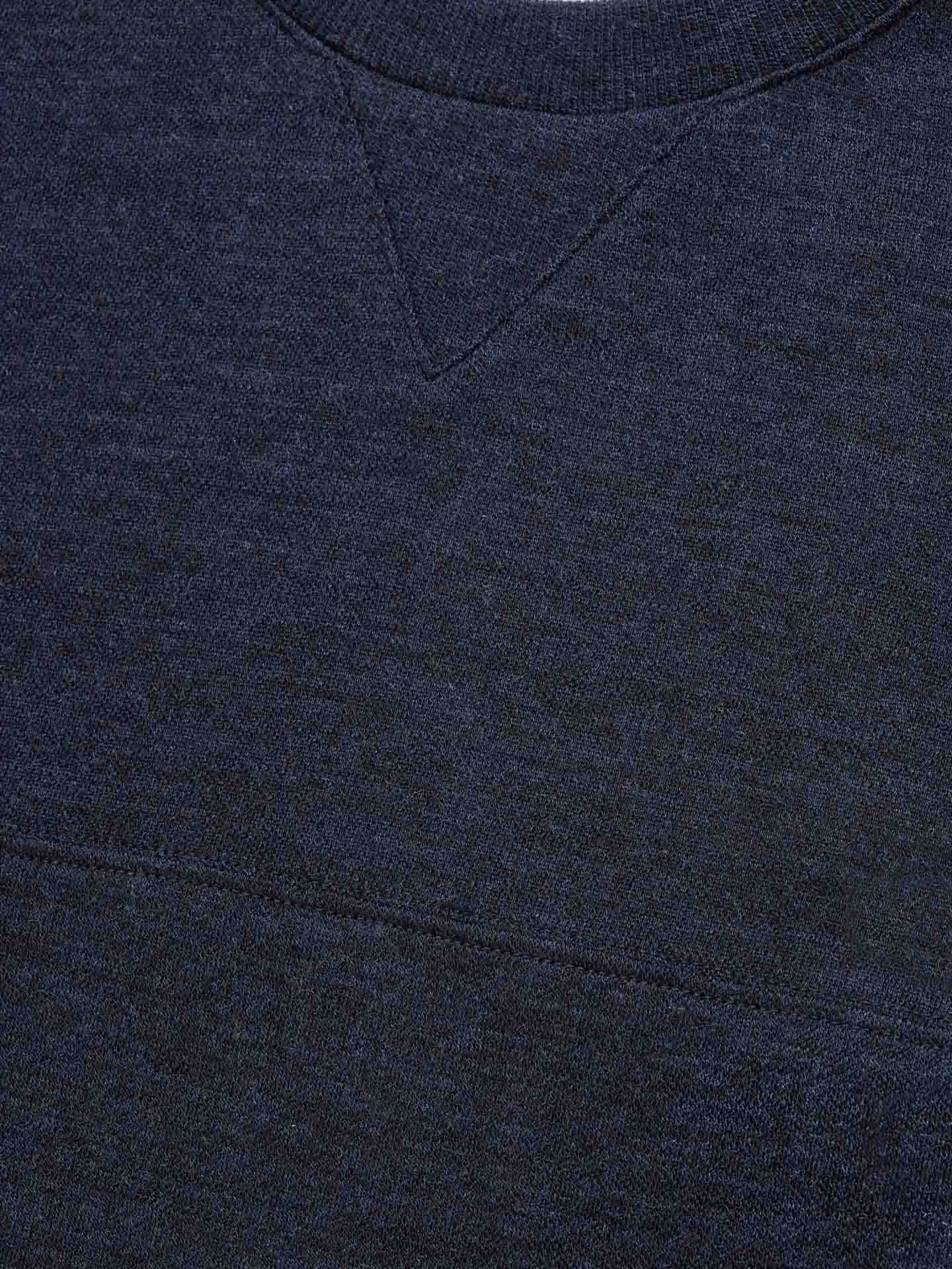 Close-up view of a dark blue, textured fabric that appears to be part of the Tind Crewneck Men by We Norwegians. The soft Merino wool material showcases intricate V-shaped stitching at the neckline and a horizontal seam below it, exuding a cozy feel reminiscent of premium sportswear.