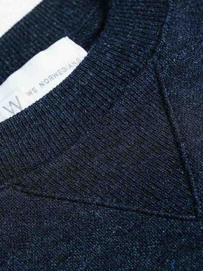 Close-up image of a dark blue Merino wool knitted fabric, showcasing the neckline and part of a clothing label with partially visible text "We Norwegians," from the Tind Crewneck Men collection.