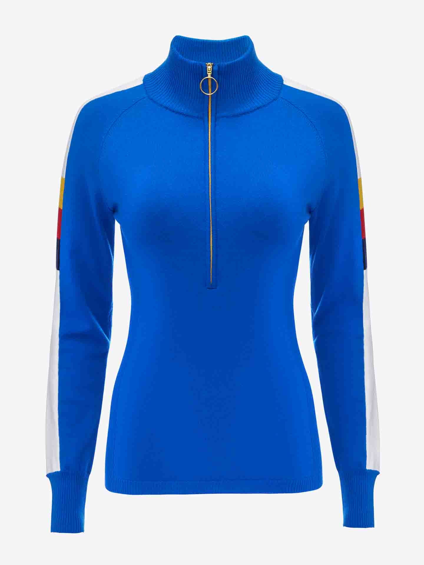 The Varden Zip Up Women by We Norwegians is a blue women's ski sweater crafted from Merino wool. It features long sleeves and a high collar with a front half-zip closure adorned with a gold ring pull. The sleeves include white side panels accented with red, yellow, and black near the shoulders, giving it a 70s-inspired look.