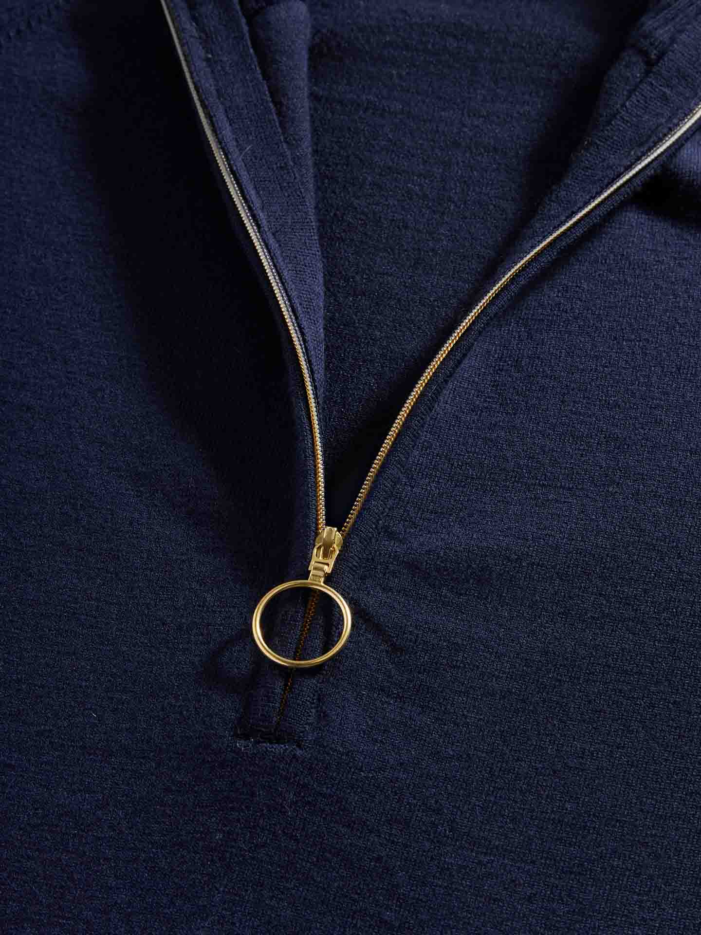 Close-up image of the Varden Zip Up Women by We Norwegians in navy blue, featuring a gold zipper. The zipper is partially open, revealing the texture of the fabric. The circular ring zipper pull adds a stylish detail to this 70s inspired garment.