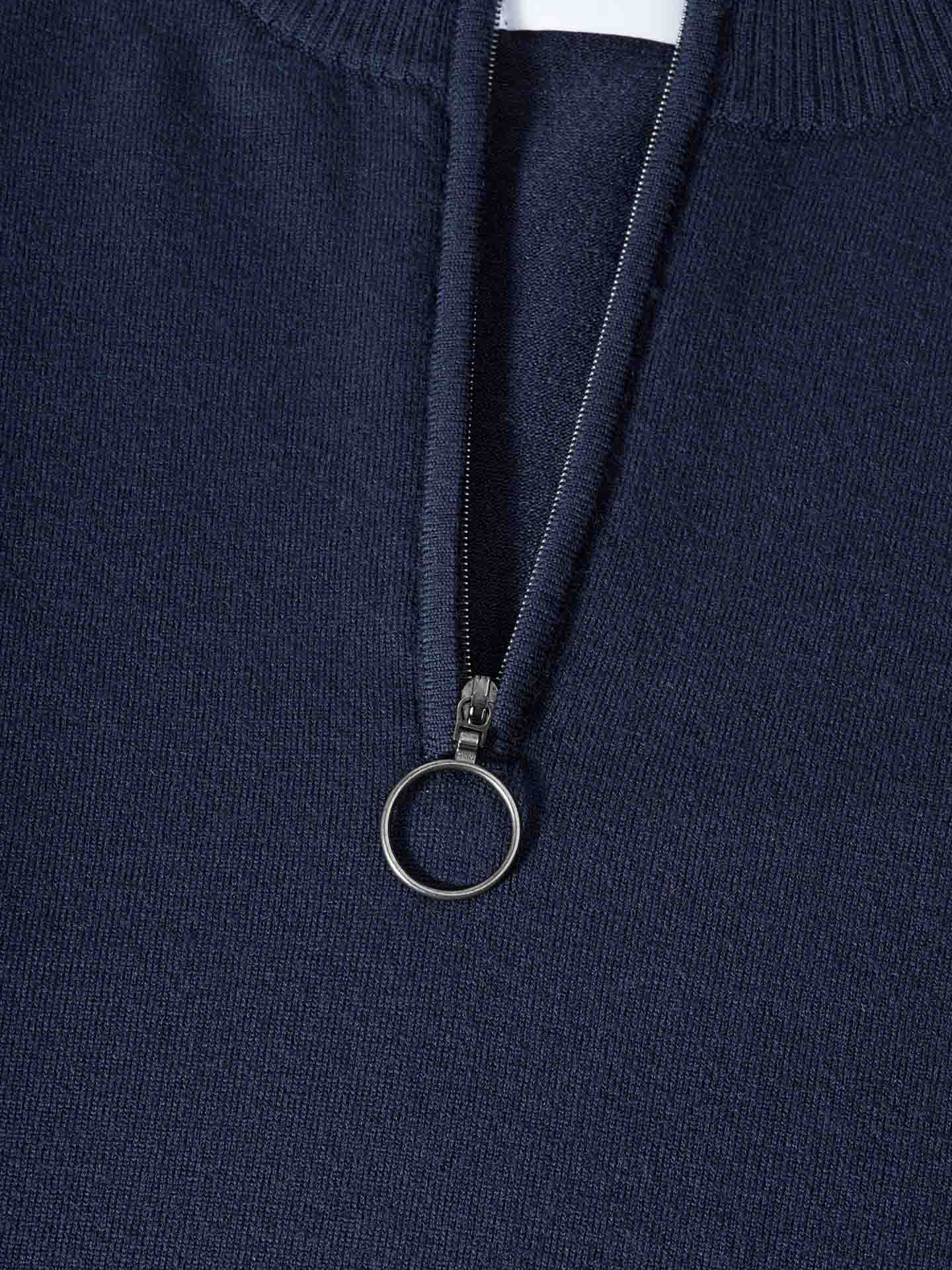 A close-up of the Varden Zip Up Men from We Norwegians, featuring a navy blue color and a silver ring pull on the zipper. The fabric texture is visible, revealing luxurious Merino wool with a ribbed collar. The collar is slightly open, uncovering the inner lining of this elegantly crafted piece made in Italy.