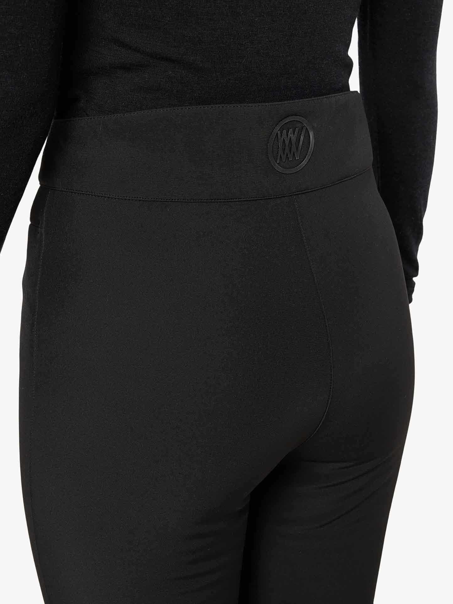 A person wearing the We Norwegians Tyin Bootleg Ski Pant Women, which features a wide waistband with an embossed logo on the back center of it. The simple and unobtrusive background further accentuates the sleek design reminiscent of ski sweaters.