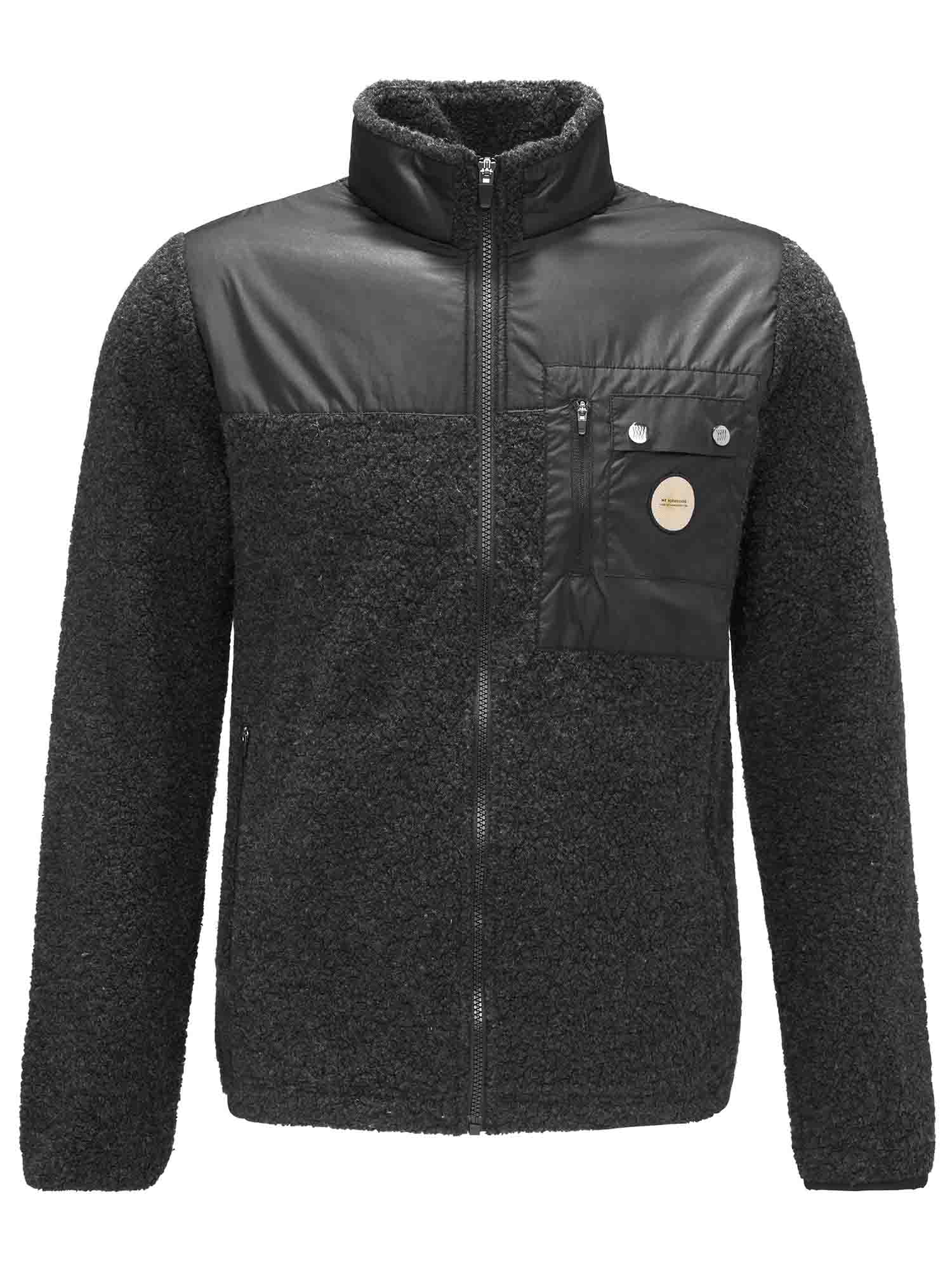 This image shows the We Norwegians Alta Jacket Men, a dark gray fleece jacket with a high collar and a front zipper. Perfect for outdoor activity, it features a contrasting black panel on the chest with a small pocket adorned with buttons and a round logo. Part of the Alta collection, its sleeves and lower body maintain a consistent fleece texture.