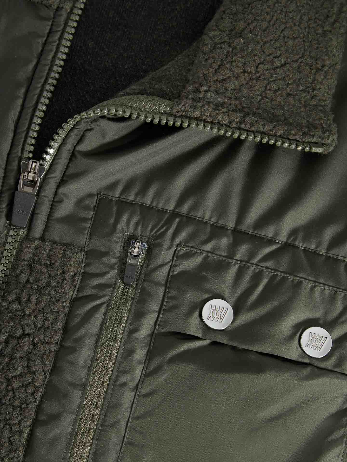 Close-up of a We Norwegians Alta Jacket Men in green with the front zipper partially undone, revealing a black inner layer. This jacket showcases a blend of smooth and textured fabric, featuring a sherpa-lined collar. Snaps and zippered pockets complete this Merino wool design tailored for outdoor activities.