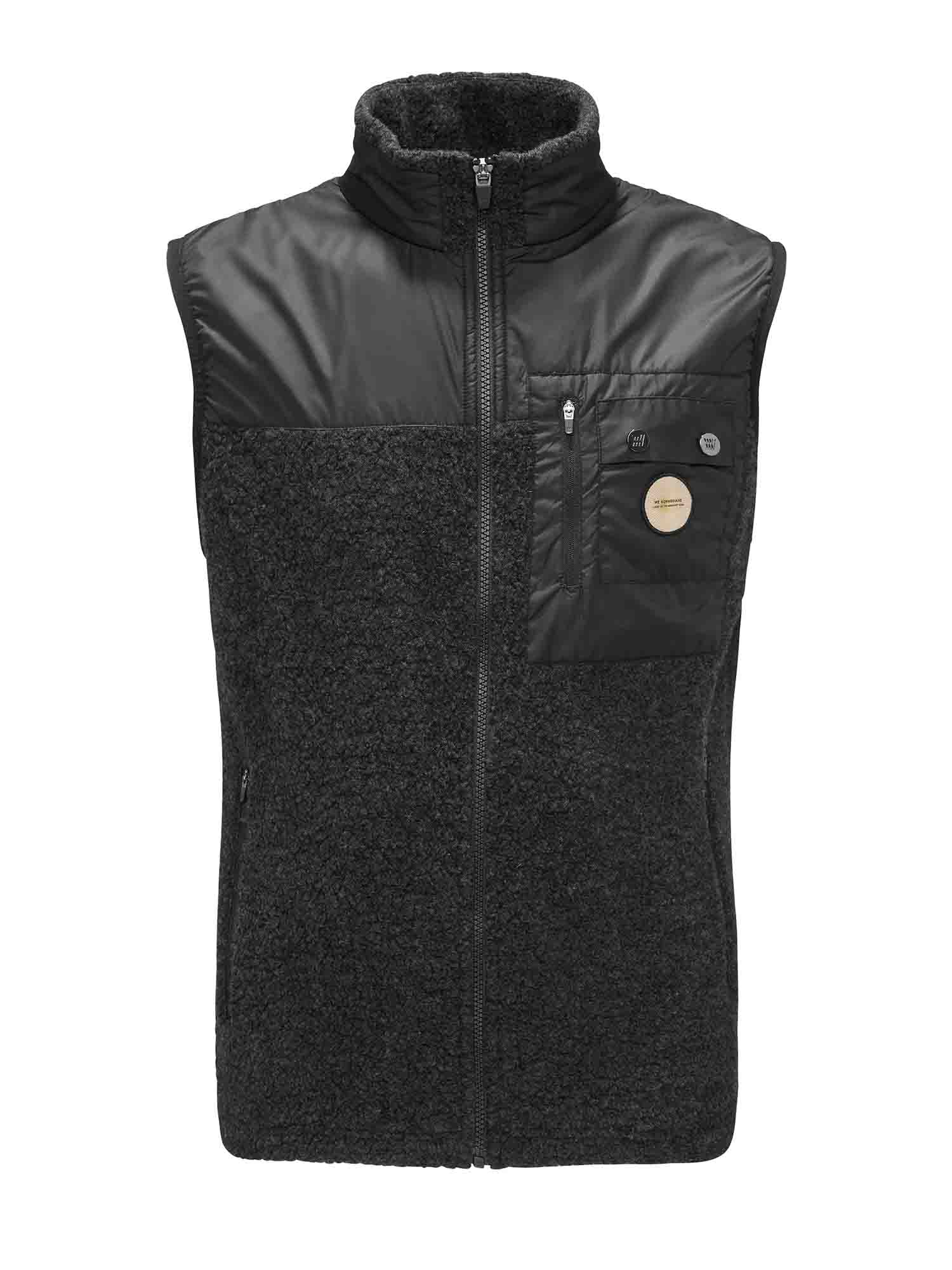 The Alta Vest Men by We Norwegians is a sleeveless, zip-up black vest with a high collar that's perfect for outdoor activities. The top portion and chest pocket are crafted from a smooth, shiny material, while the rest features a contrasting fuzzy fabric. The chest pocket has a zip closure and two small patches—one round and one square.