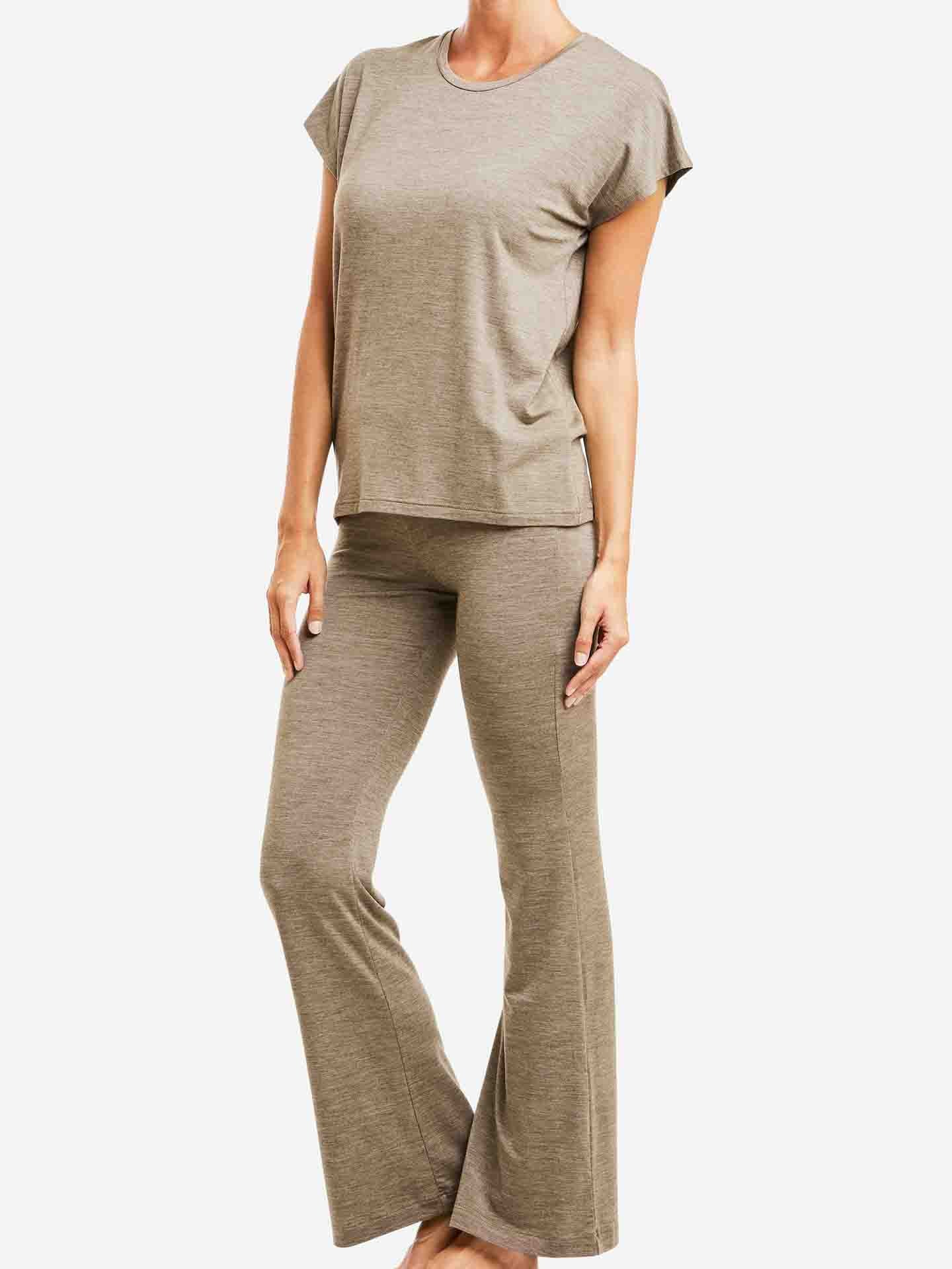 A person is wearing a beige, short-sleeved HYGGE base layer and matching Hygge Flared Pant for women by We Norwegians. They are barefoot and standing against a plain white background.