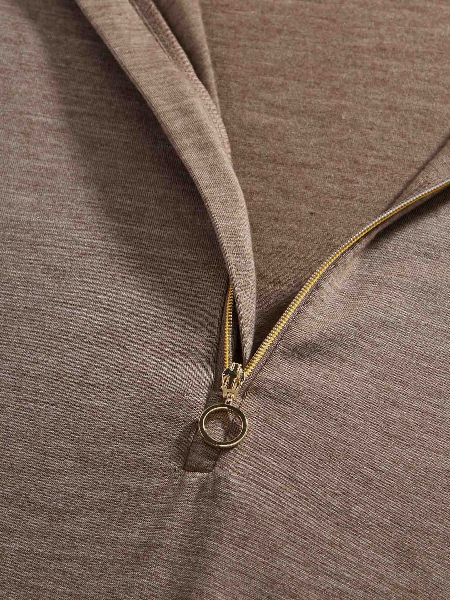 Close-up of the Hygge Zip Up Women by We Norwegians in light brown, featuring a partially open gold zipper near the collar. The zipper has a round pull tab, and the soft, slightly textured fabric evokes the cozy comfort of a hygge base layer.