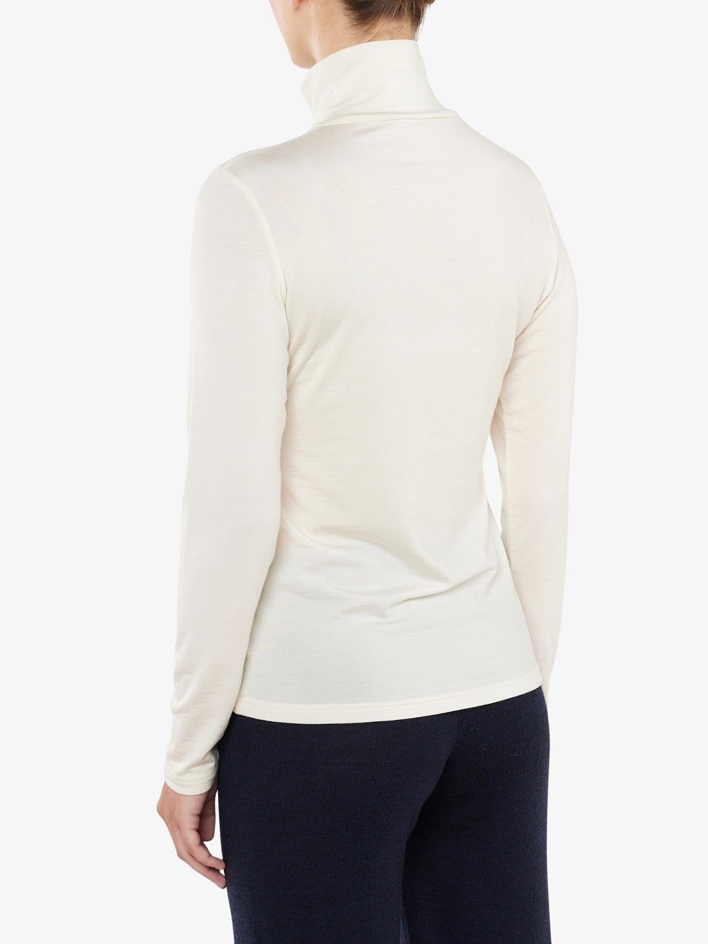 A person facing away from the camera is wearing a cream-colored Hygge Zip Up Women shirt made of Merino wool by We Norwegians and dark pants. The plain white background highlights the luxury base layer and the back view of the person.