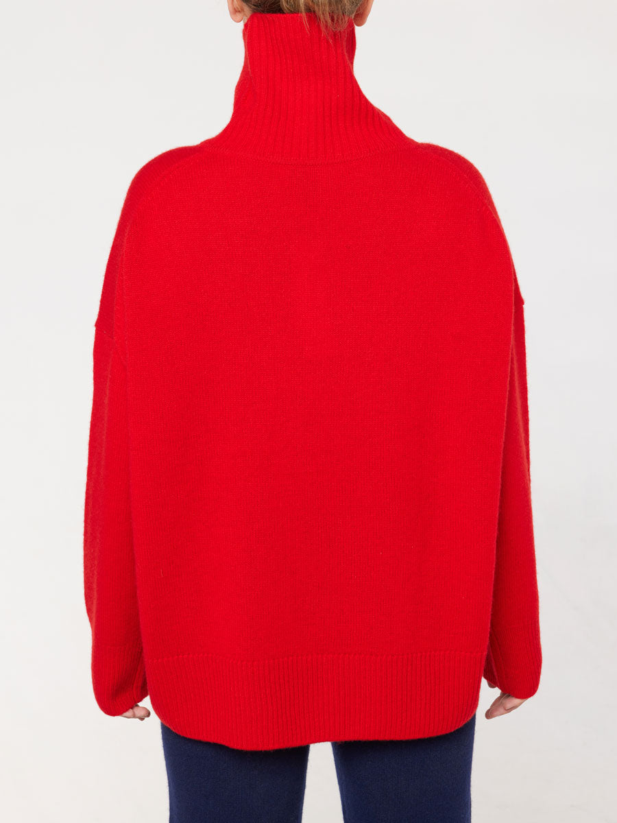 A person is shown from behind wearing a vibrant red Blefjell Sweater Women by We Norwegians. The oversized fit with long sleeves and the person's hair tied up reveals the high neckline. The background is plain white.