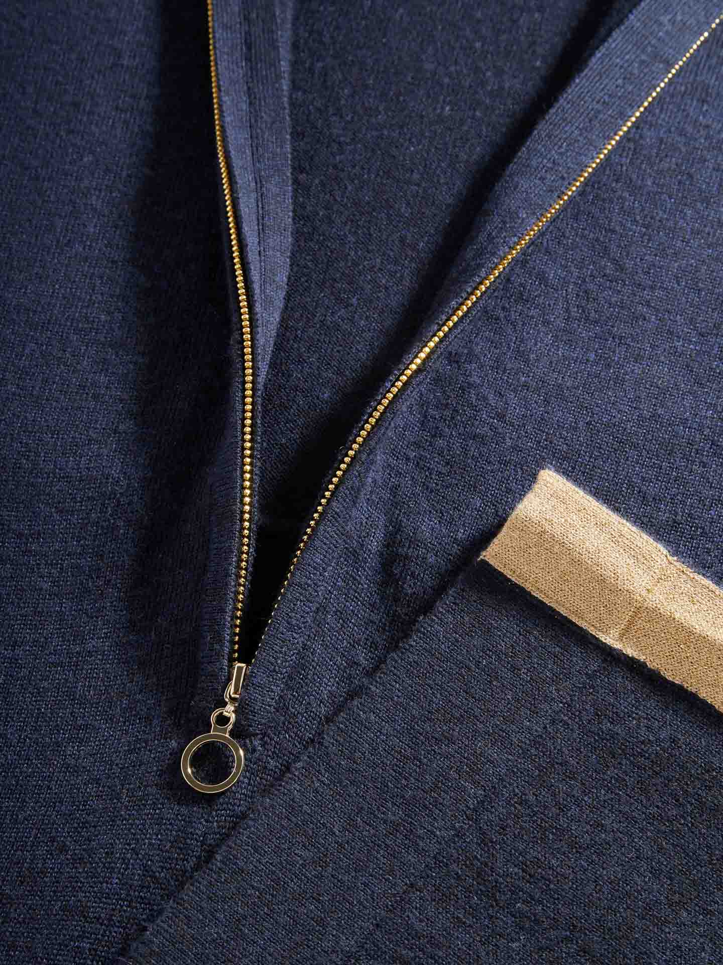 Close-up of the We Norwegians Geilo Jumpsuit for Women in dark blue featuring a partially open metallic zipper with a round pull tab. A beige strap or tag is attached to an adjacent seam. The material, reminiscent of Merino Wool, has a textured, knit-like appearance, perfect for that chic mountain resort look.