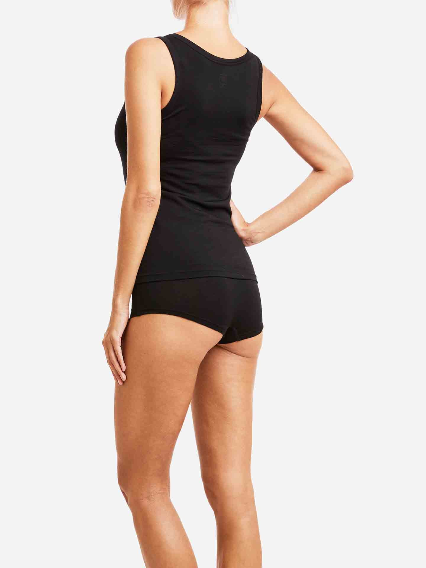 A person is standing against a white background, seen from the back. They are wearing the Sno Merino Tank Top Women by We Norwegians paired with black underwear made from super fine merino wool. The individual's arms are relaxed by their sides, exuding comfort and Scandinavian luxury base-layer elegance.