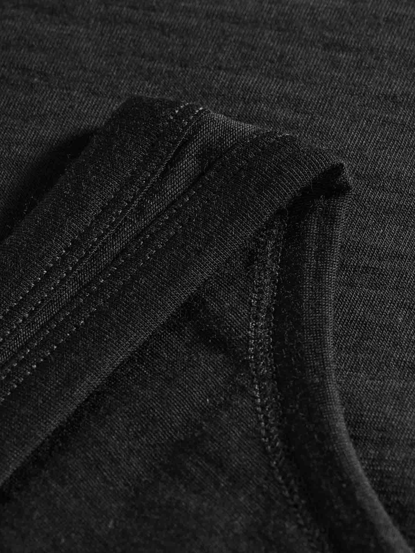 Close-up of a neatly folded black fabric, showcasing the detailed stitching and texture of the material. The fabric, made from super fine merino wool, appears to be the Sno Merino Tank Top Women by We Norwegians, possibly a fitted t-shirt, displayed on a dark background.