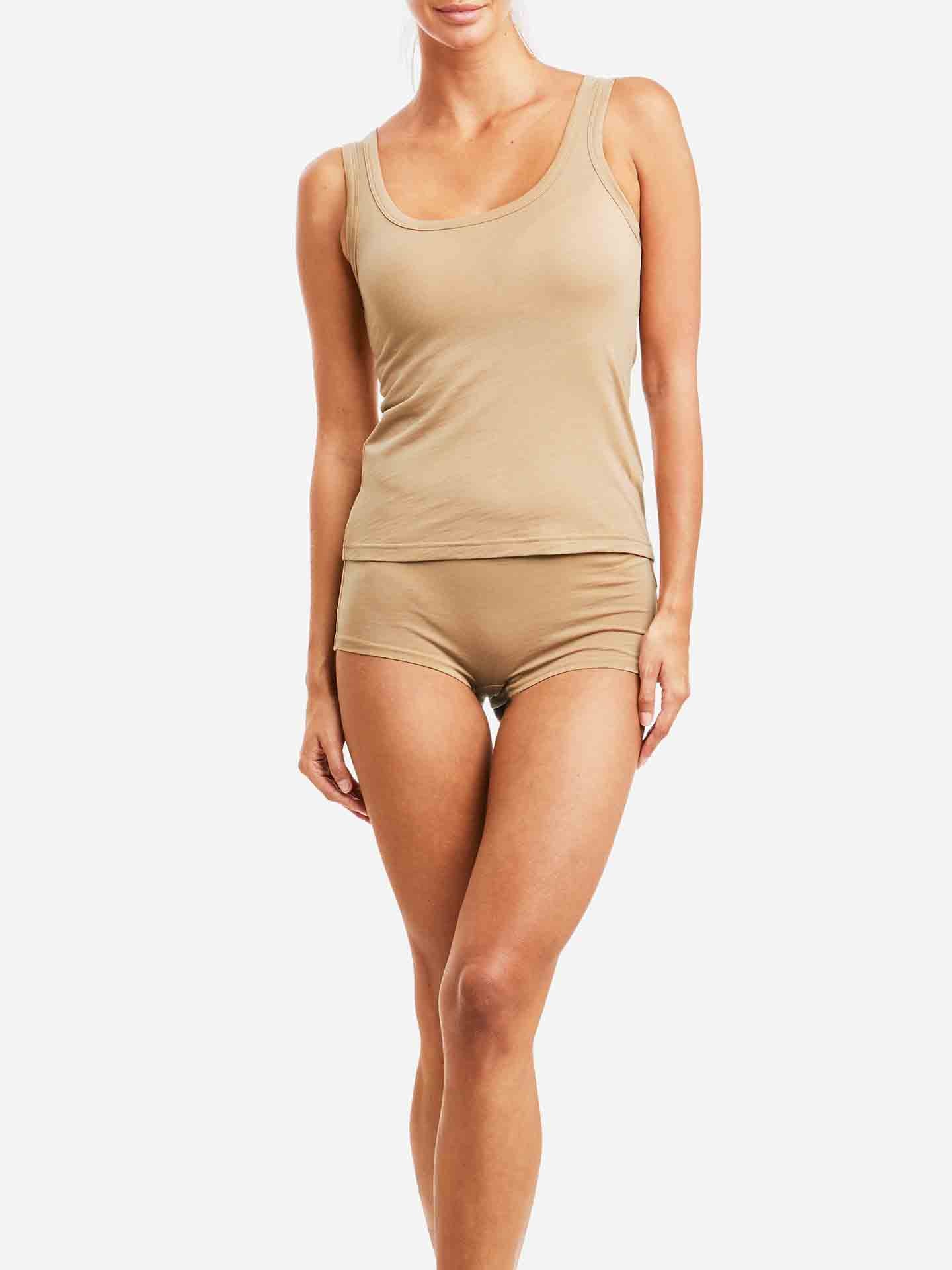 A person is wearing the Sno Merino Tank Top Women from We Norwegians, paired with matching beige shorts. The set is crafted from super fine merino wool and has a form-fitting, casual look. Against a plain white background, the person stands with a relaxed posture.