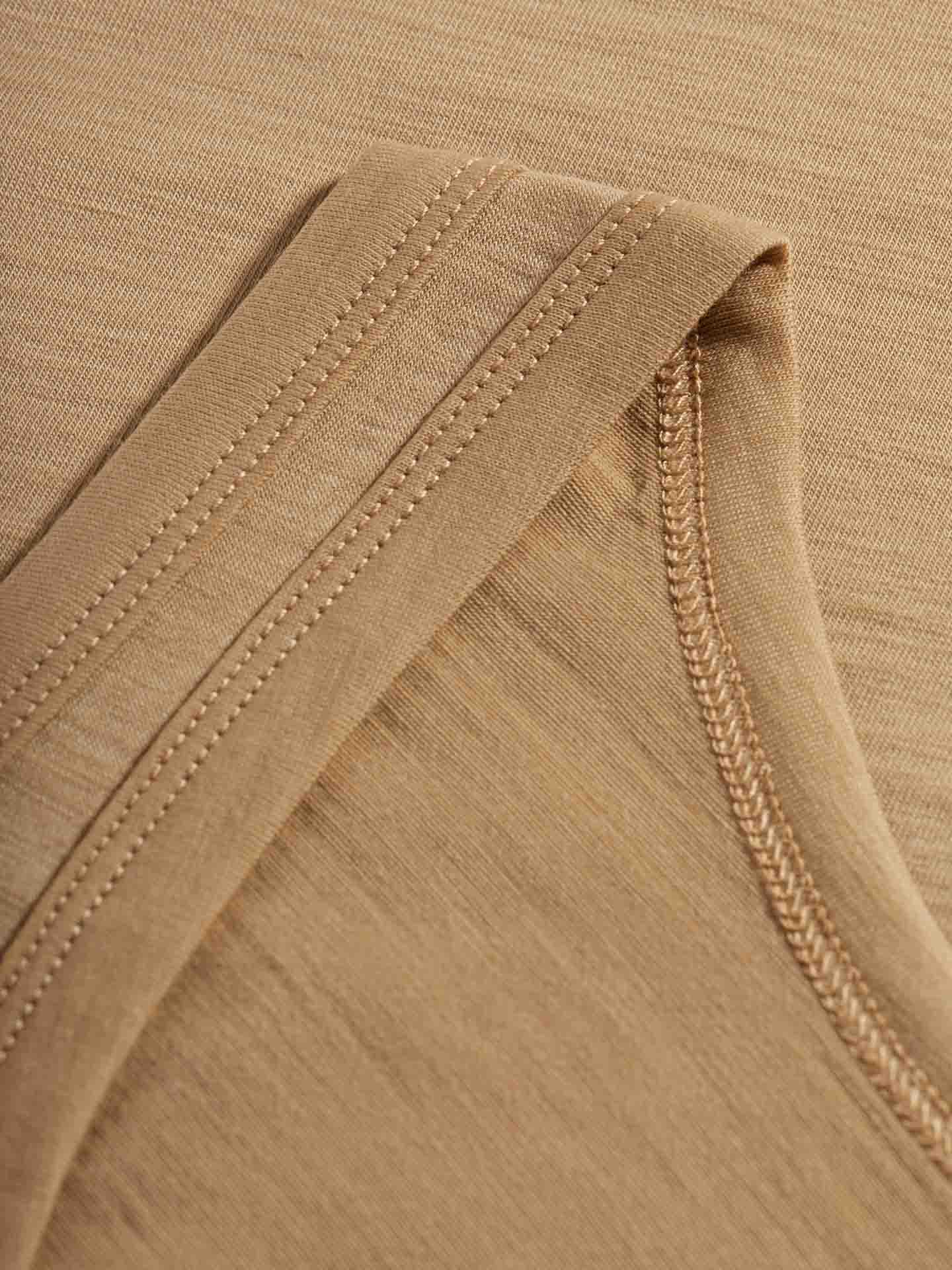 Close-up of the beige fabric on the Sno Merino Tank Top for Women by We Norwegians, featuring detailed stitching. The focus is on the seam and hem, showcasing the texture and quality of the material, reminiscent of Scandinavian luxury base-layer standards.