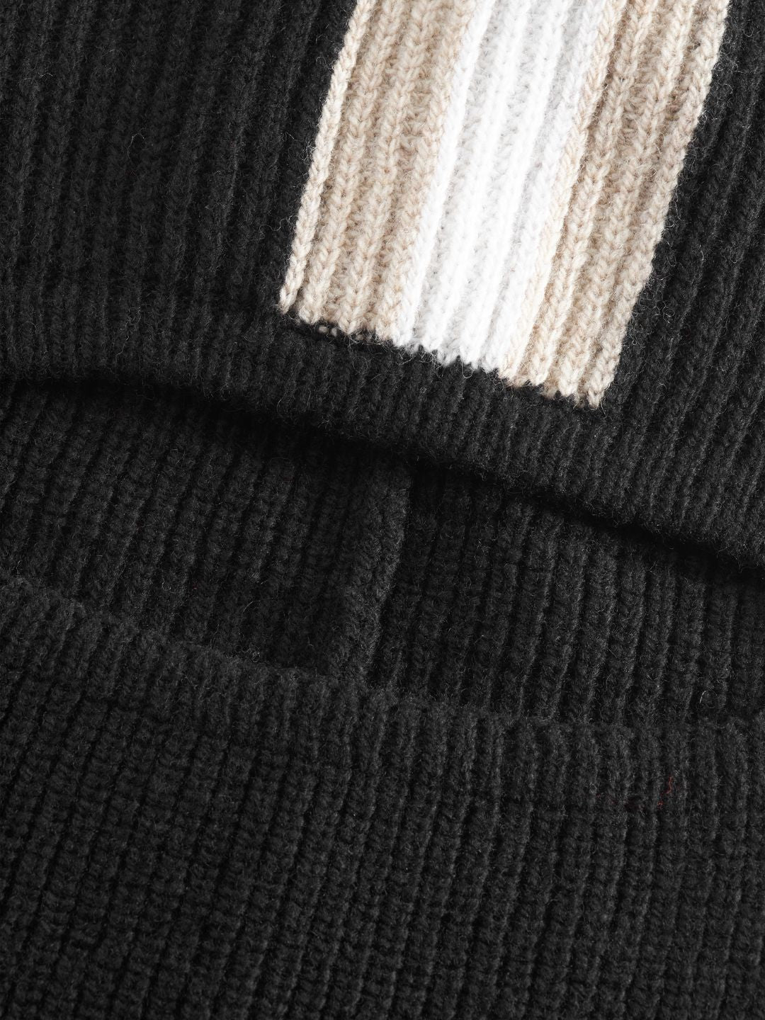 Close-up of the Apres Ski Balaclava by We Norwegians, showcasing a section of knitted black merino wool fabric with ribbing, overlain by another piece featuring a cream and beige stripe pattern. Reminiscent of 70s ski fashion, the textures and patterns of the knit are clearly visible in the image.