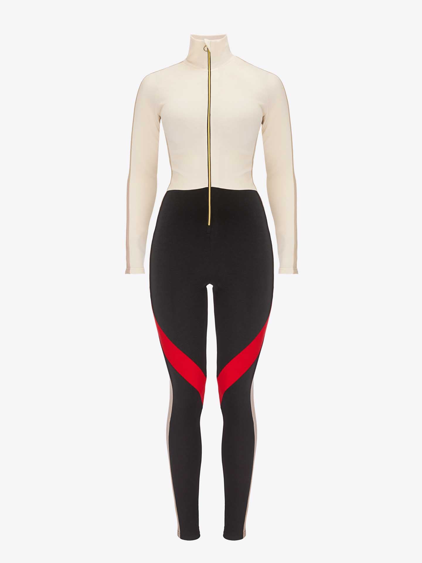 The INUIKII + WN Jumpsuit Women by We Norwegians is a full-length, long-sleeve Merino jumpsuit. It features a cream-colored top with a front zipper, complemented by black leggings with red and pink diagonal accents on the thighs. This ensemble is ideal for ski fashionistas looking for a sleek and modern style.