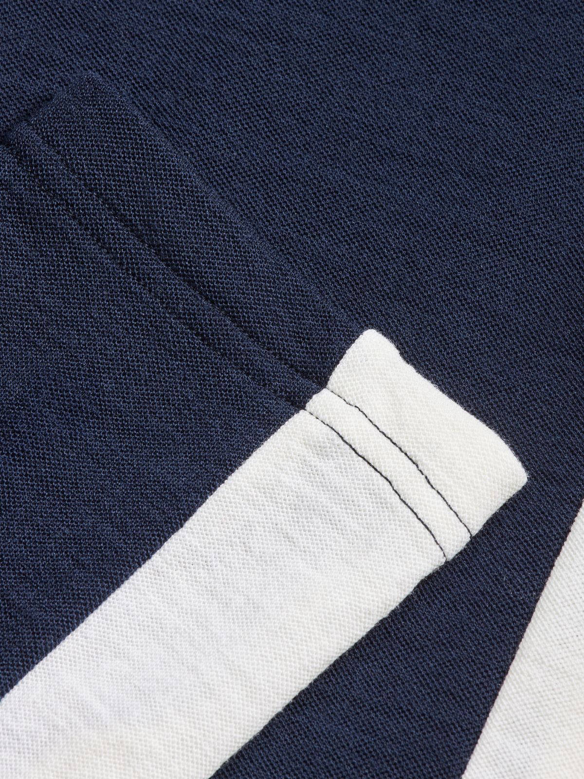 Close-up of a navy blue fabric with a pocket, highlighted by a contrasting white stripe along the edge. The texture of the Merino wool in the Inuikii+WN Leggings Women by We Norwegians is visible, suggesting a durable, woven material that ski fashionistas will adore.