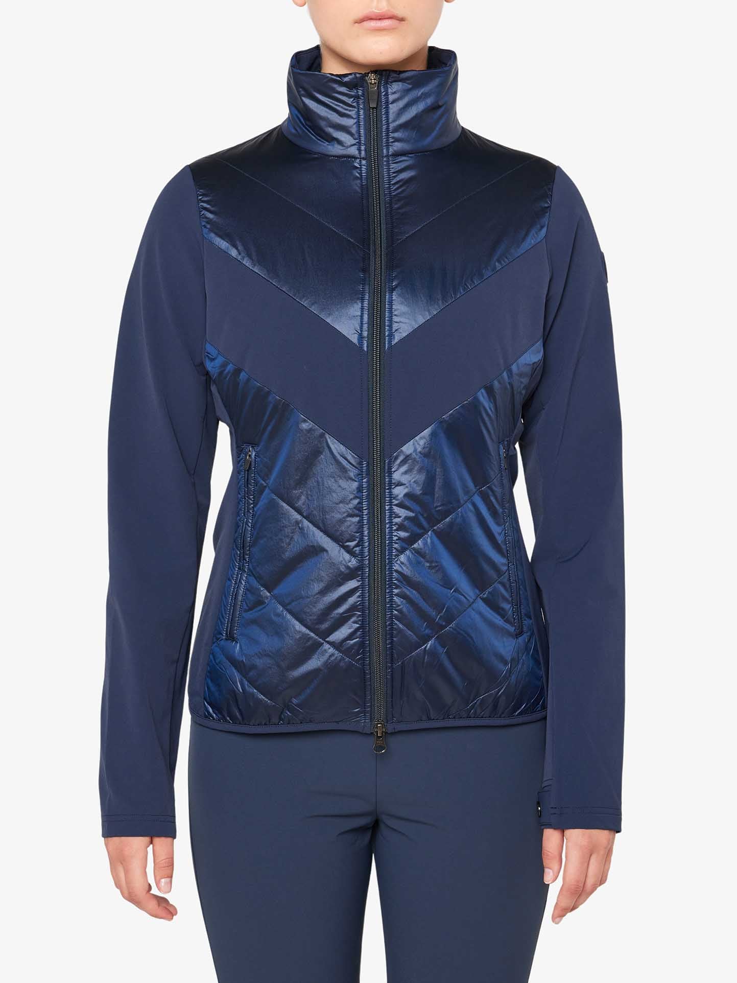 A person is wearing a navy blue Beito Jacket Women by We Norwegians, featuring a shiny, quilted front and a zippered closure. The jacket boasts a high collar and long sleeves, making it ideal for cross country skiing. Paired with matching navy blue pants, the outfit stands out against the plain white background.